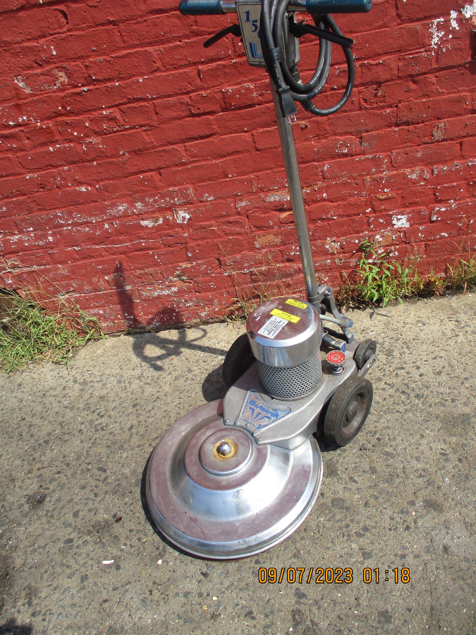 A machine is sitting on the sidewalk in front of a red brick wall.