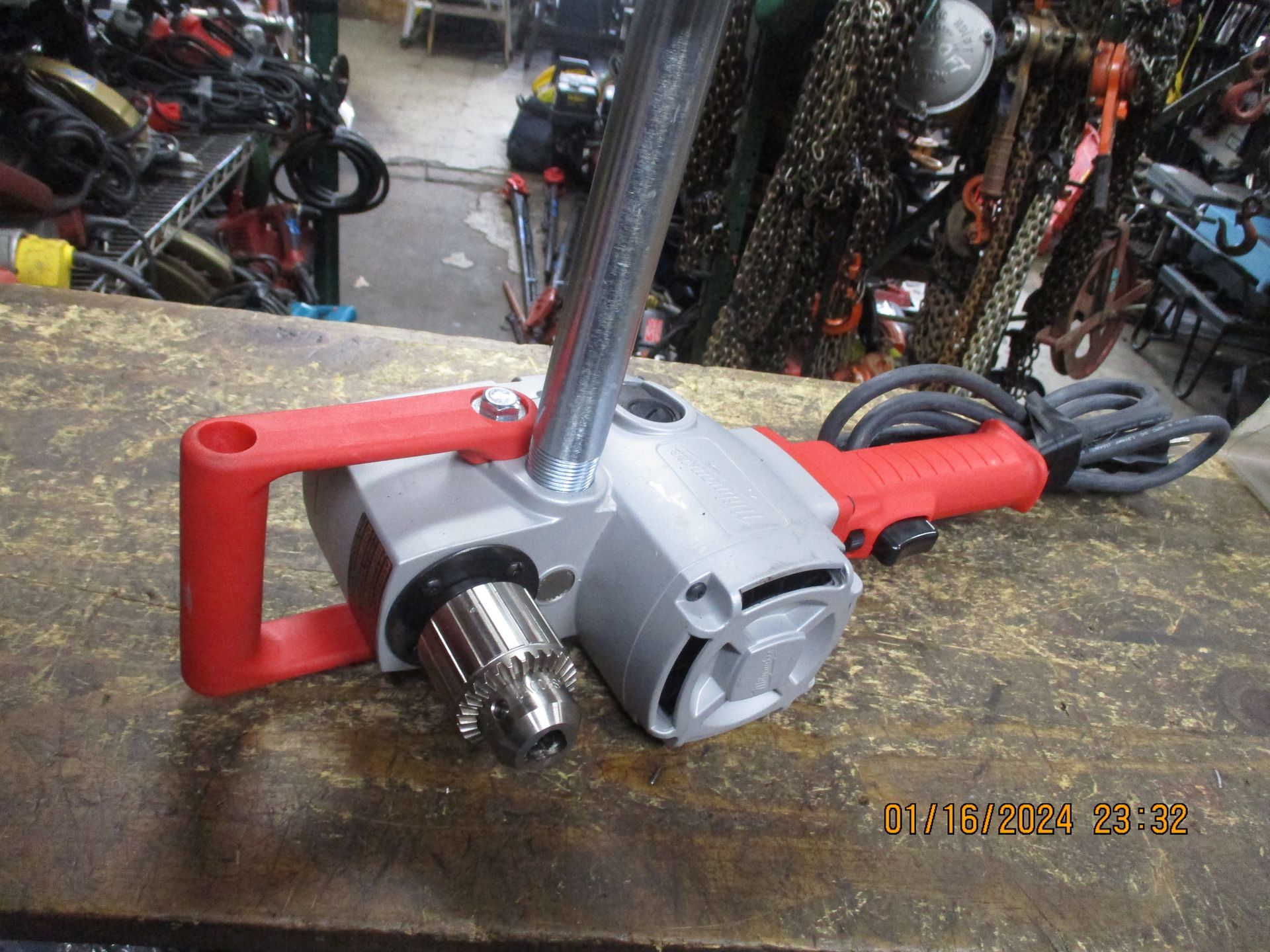 A drill with a red handle is sitting on a wooden table.