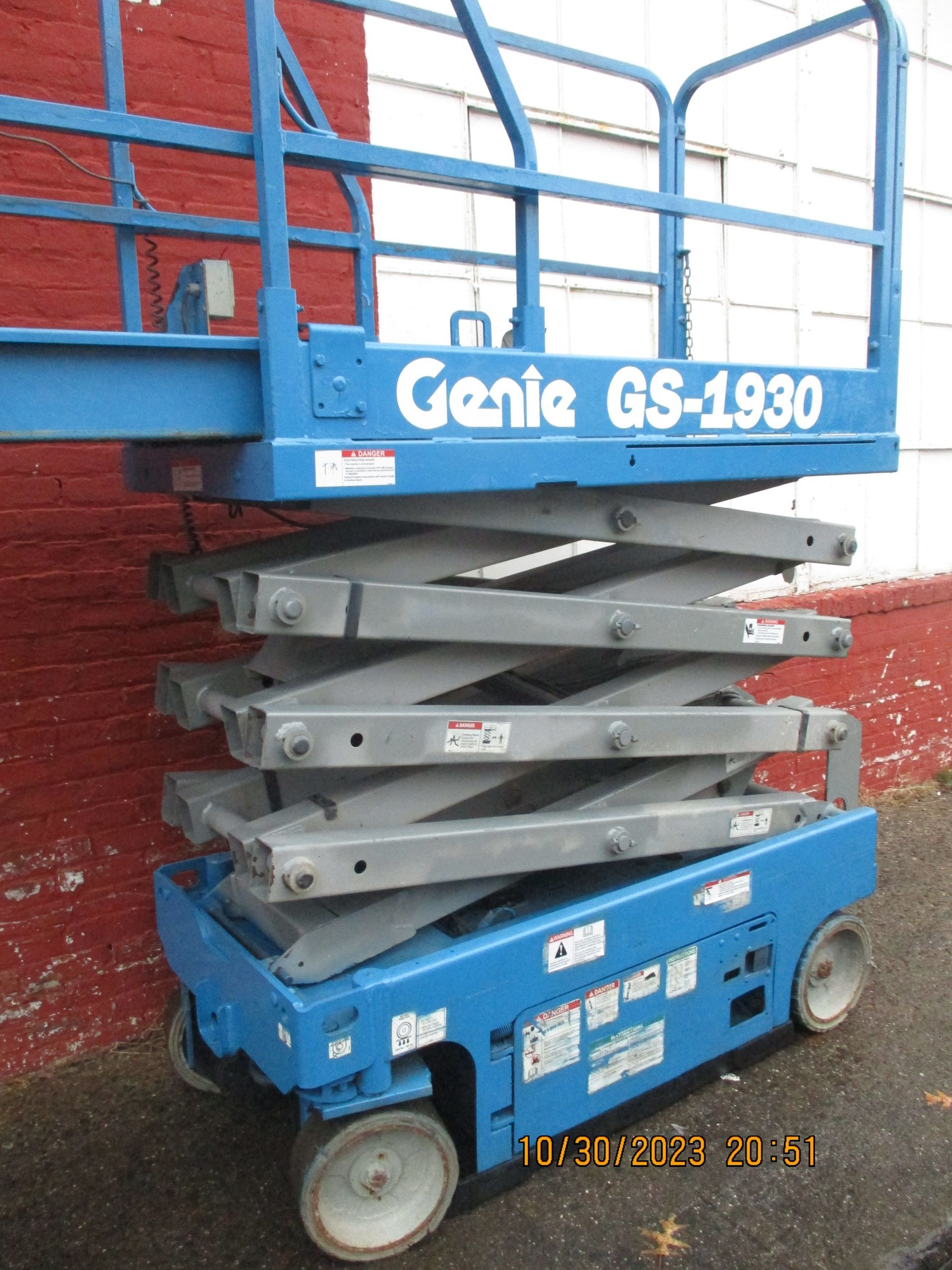 A genie gs-1930 scissor lift is parked in front of a brick wall