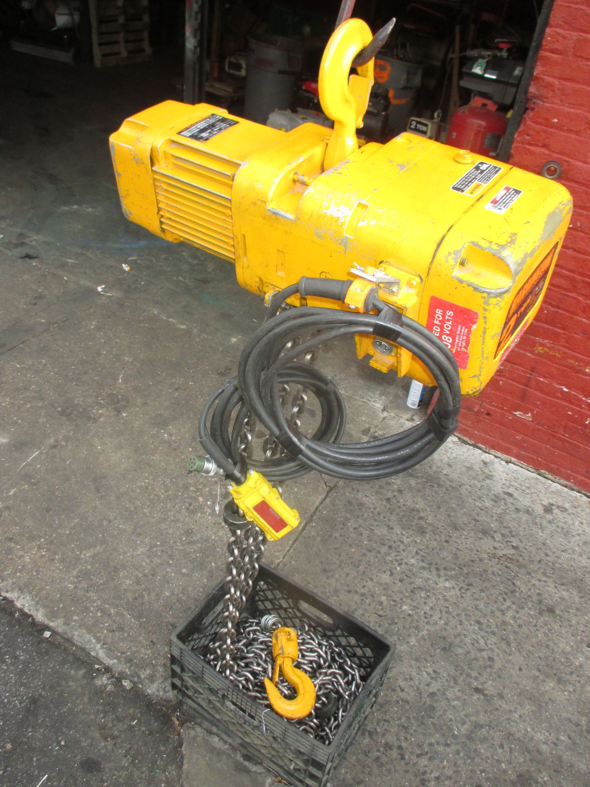 A yellow crane is sitting on a sidewalk next to a brick wall