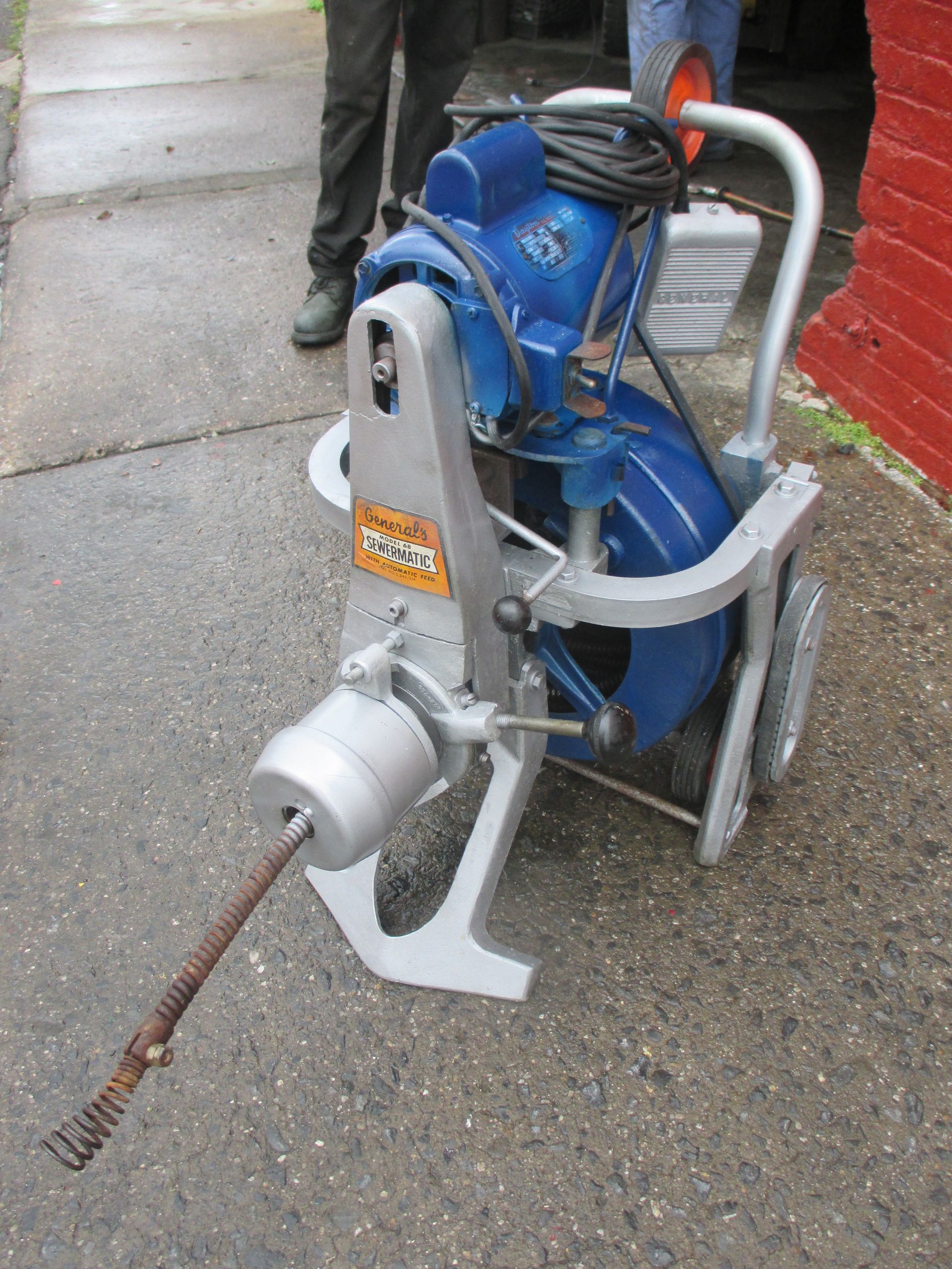 A drain cleaner is sitting on the sidewalk in front of a red brick building