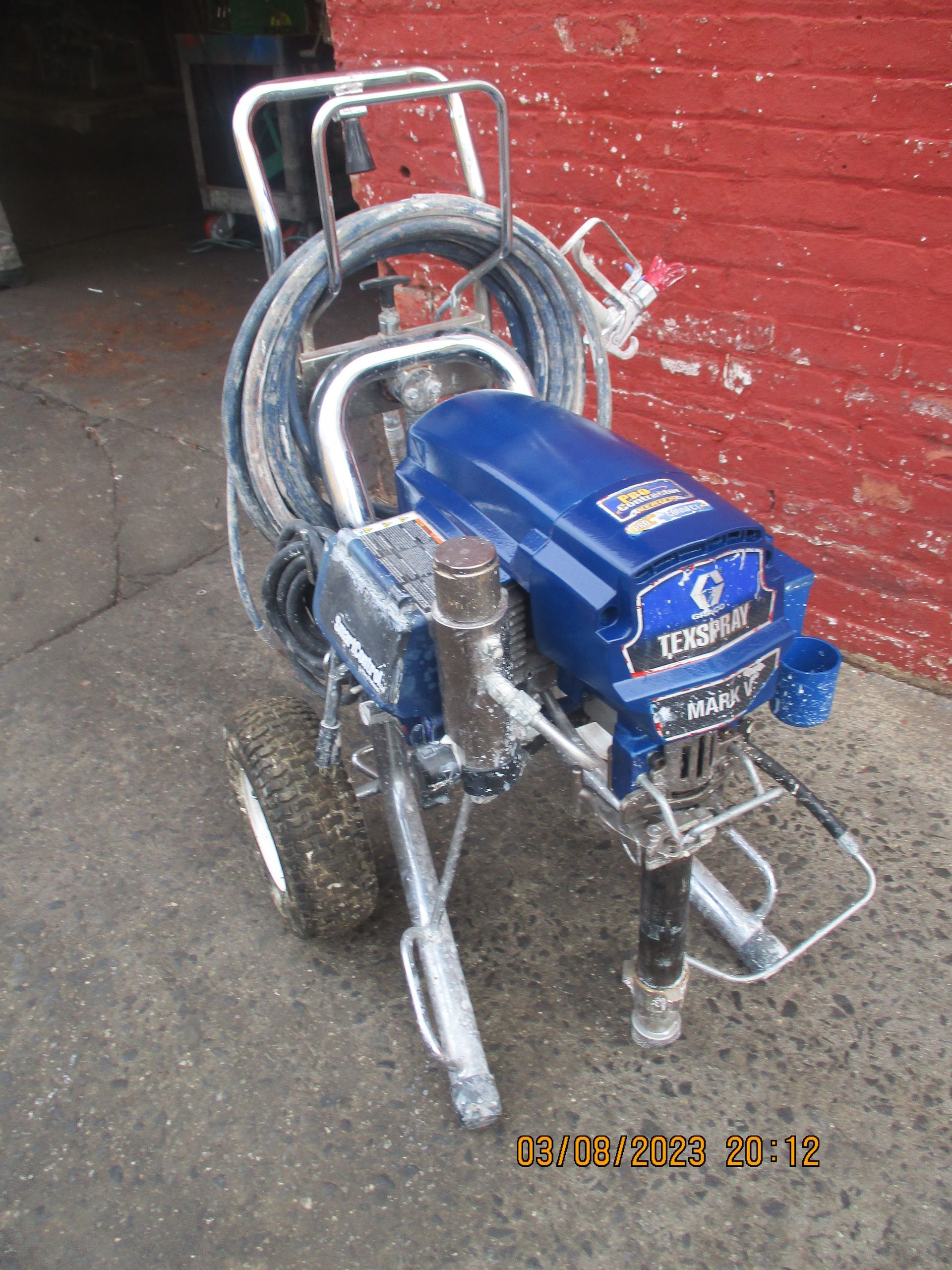 A paint sprayer is sitting in front of a red brick wall.