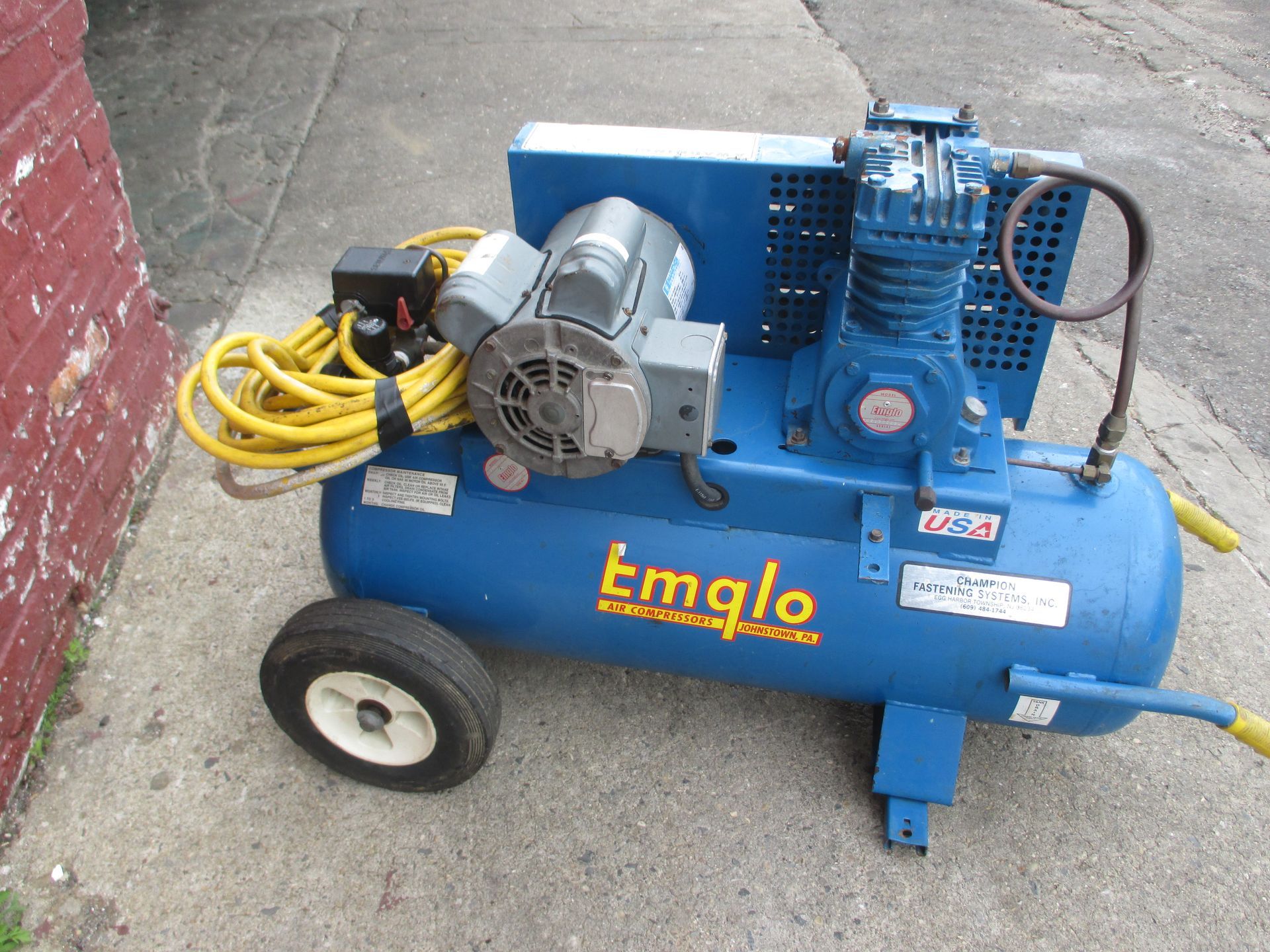 A blue emglo air compressor is sitting on the sidewalk