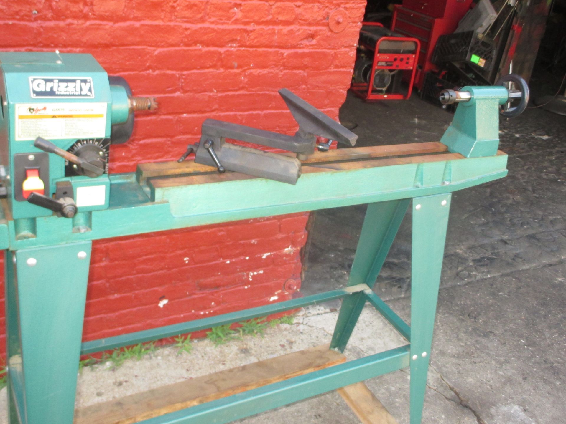 A green lathe is sitting in front of a red brick wall