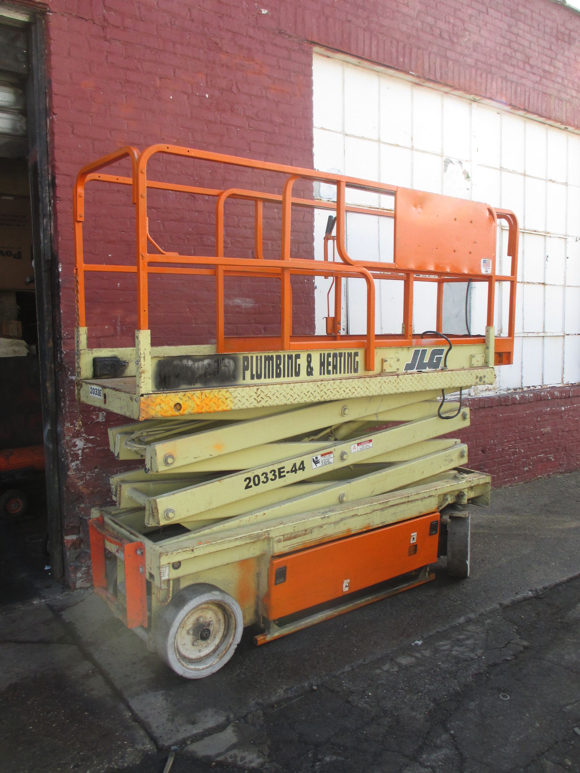 An orange scissor lift is parked in front of a brick building