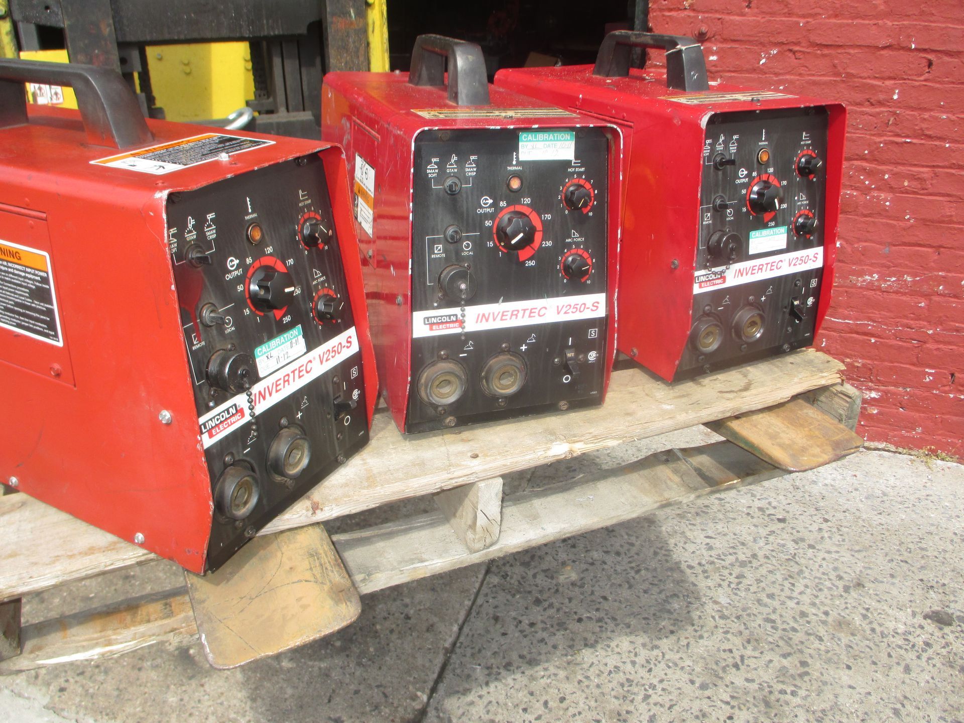 Three welding machines are sitting on a wooden pallet