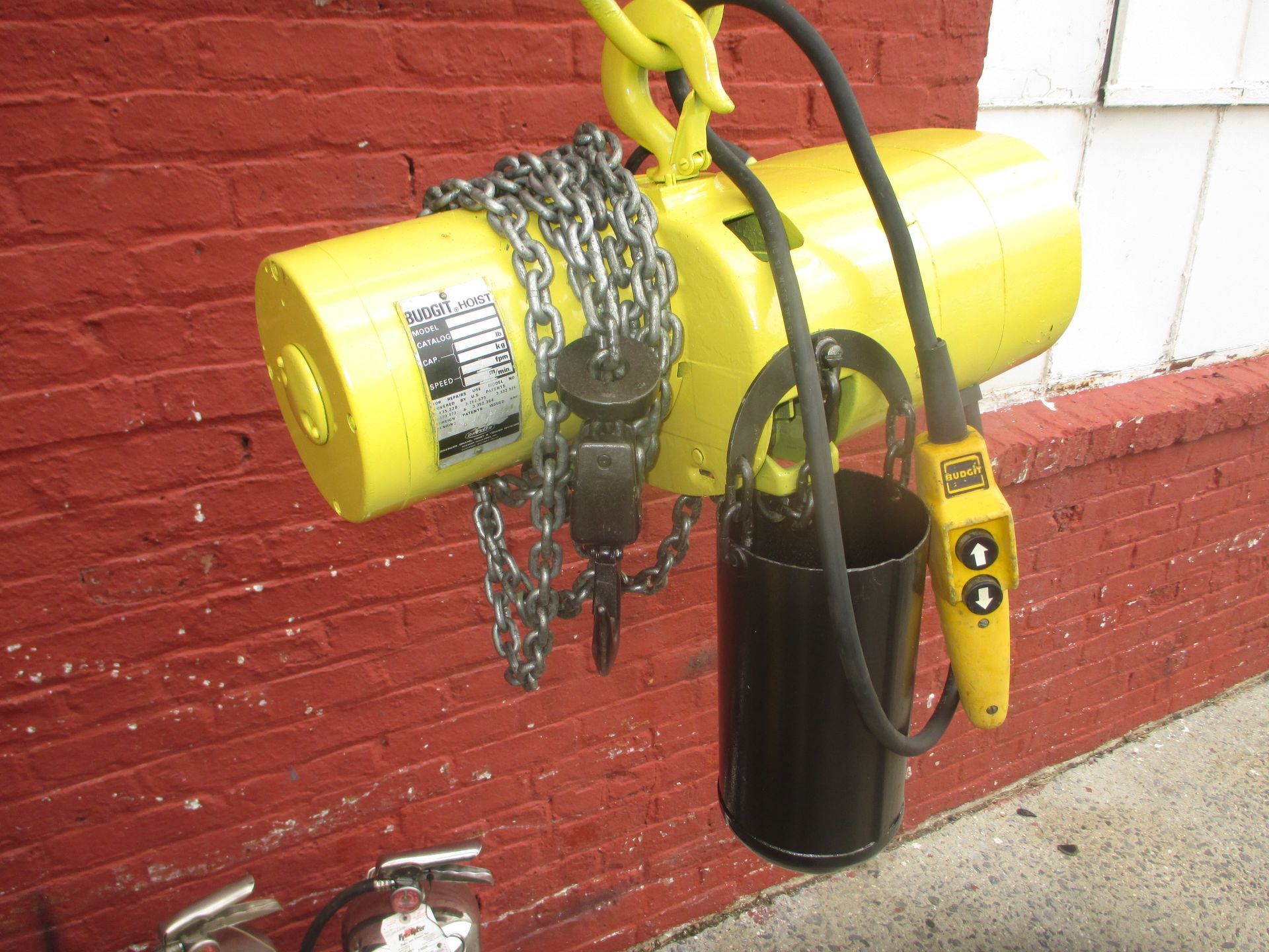 A yellow chain hoist is attached to a red brick wall