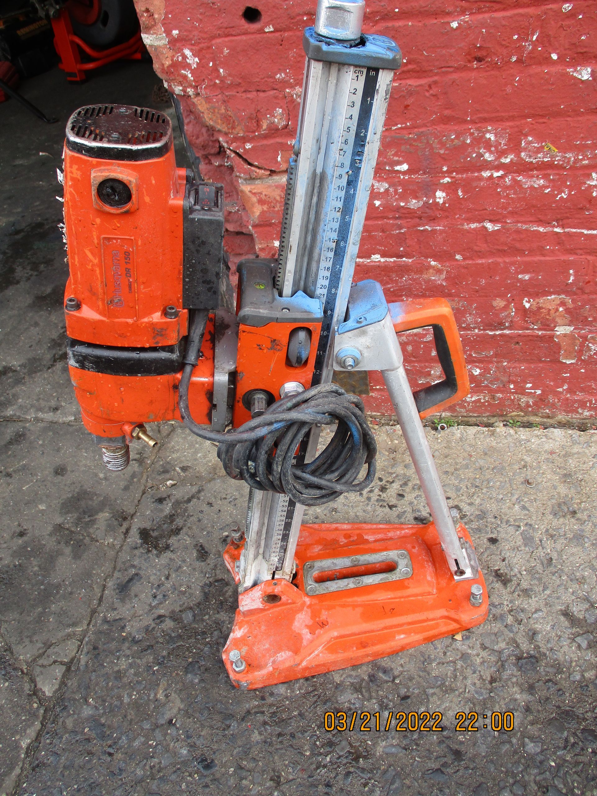 An orange machine is sitting in front of a red brick wall