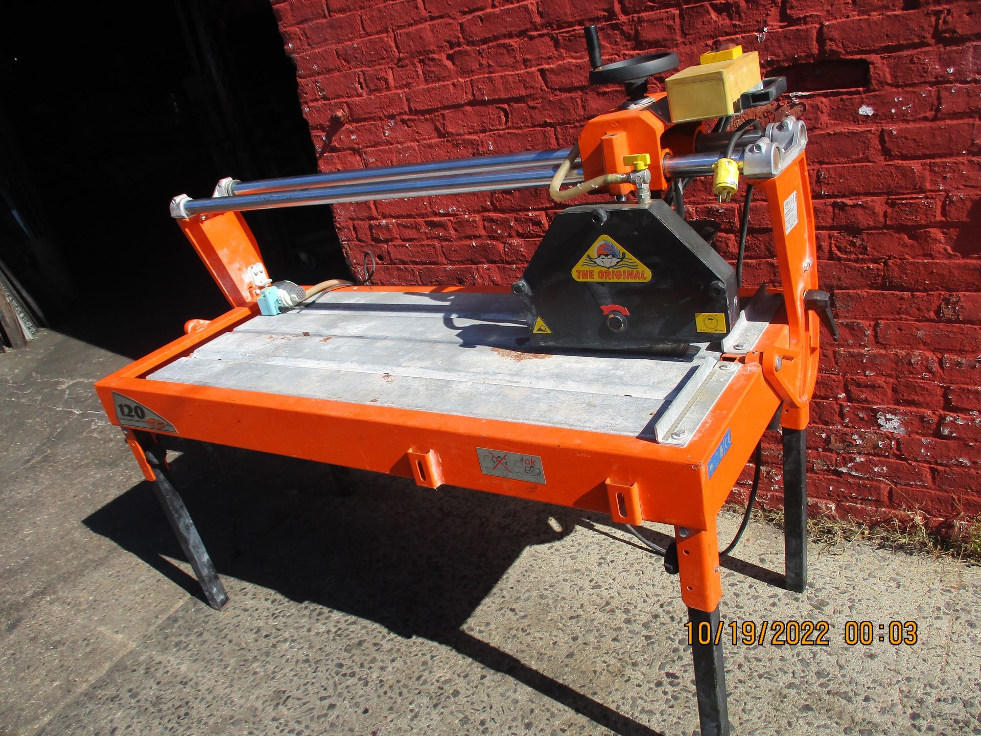 A brick wall is behind a table saw that is orange