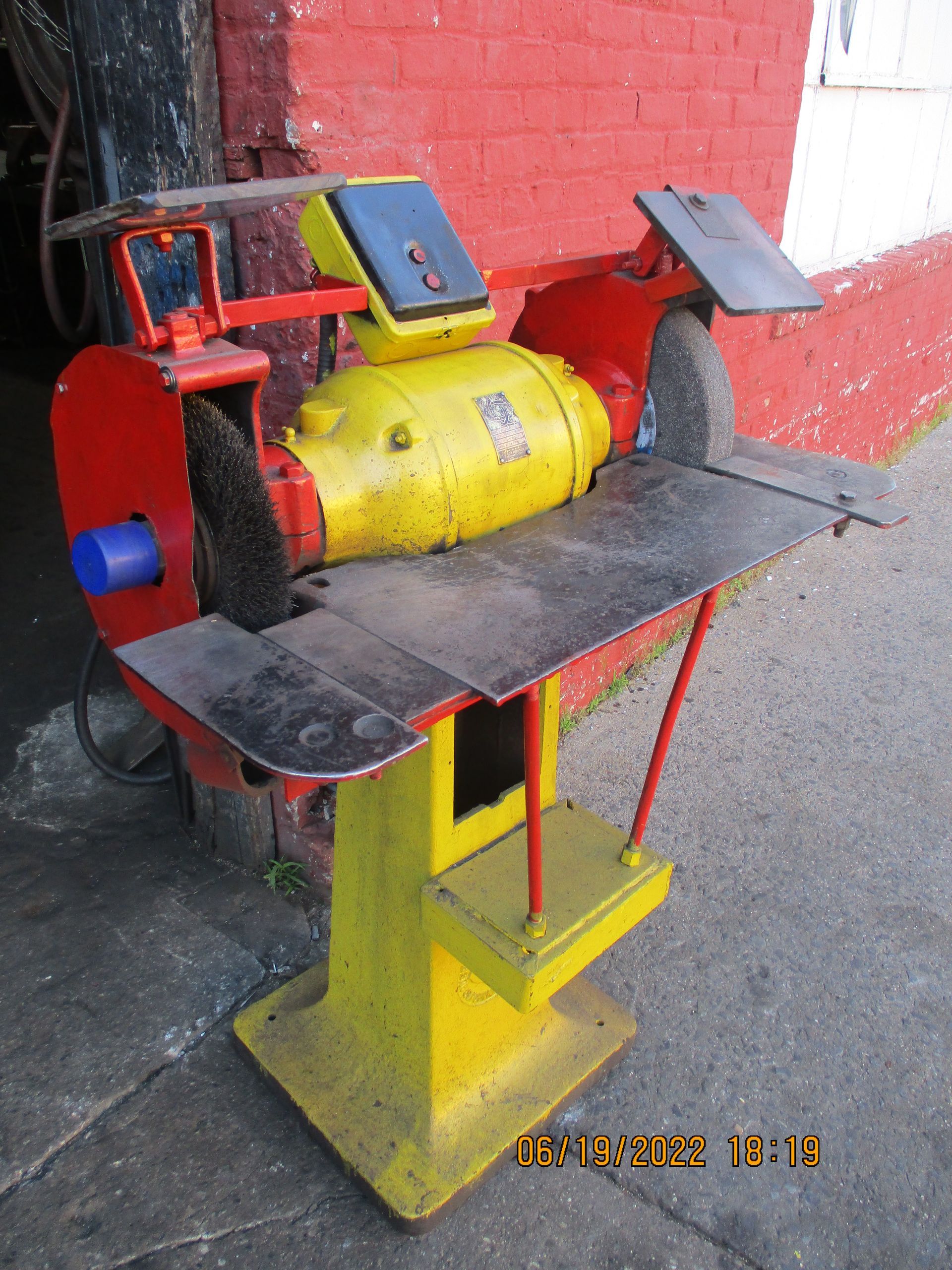 A yellow and red grinder is sitting in front of a red brick wall