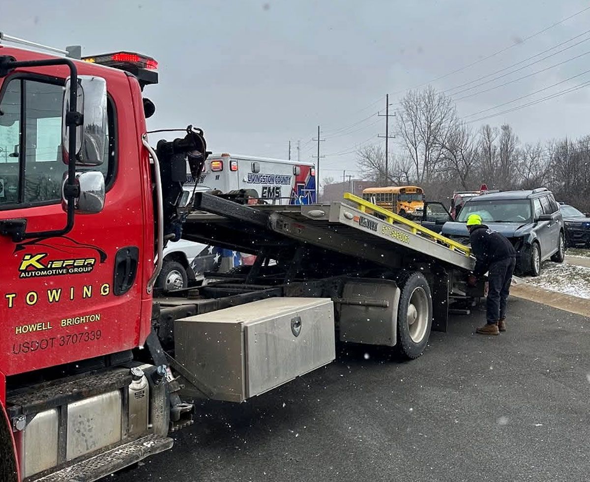 Tow truck loading a damaged car on a snowy roadside as a worker stands nearby