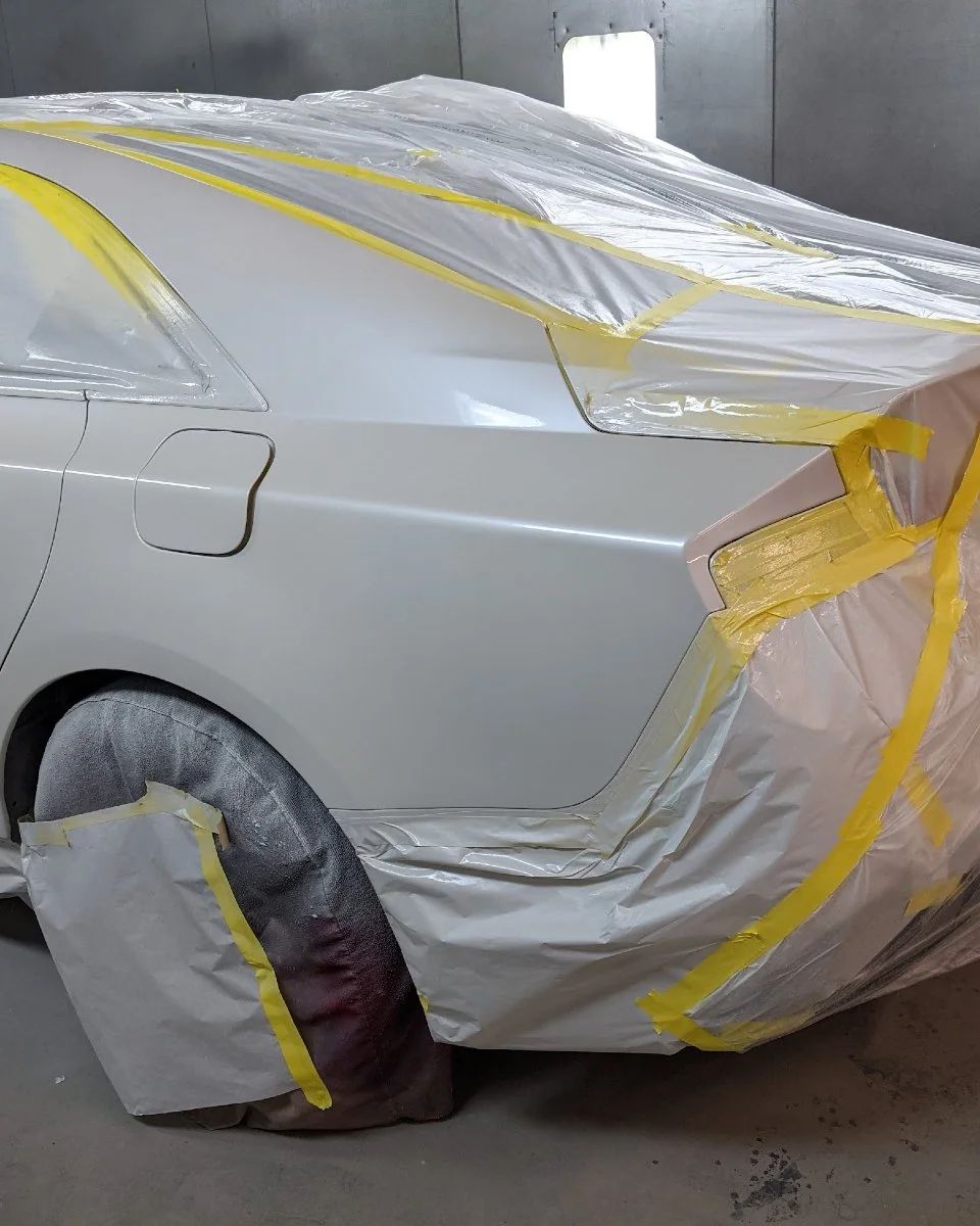 Silver car masked with yellow tape and plastic in a spray paint booth