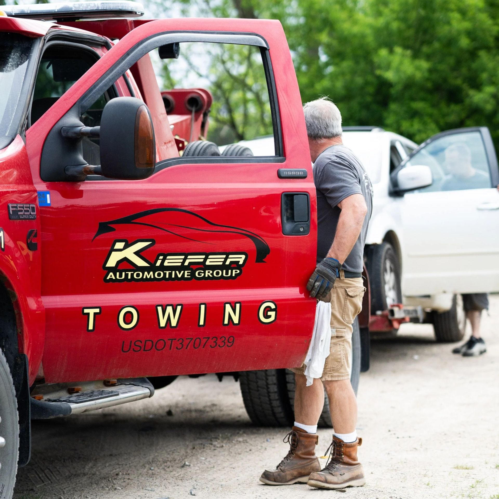 Tow truck driver beside a red towing truck assisting a white car on the roadside