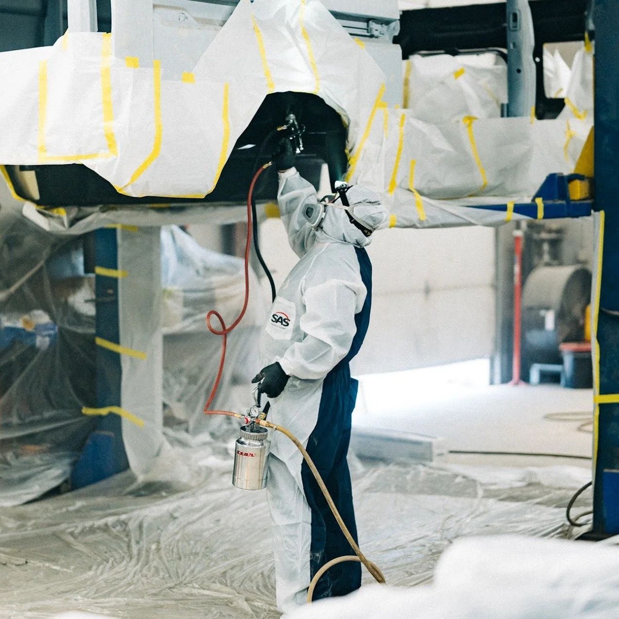 Worker spray-painting a large object wrapped in plastic in an industrial workshop