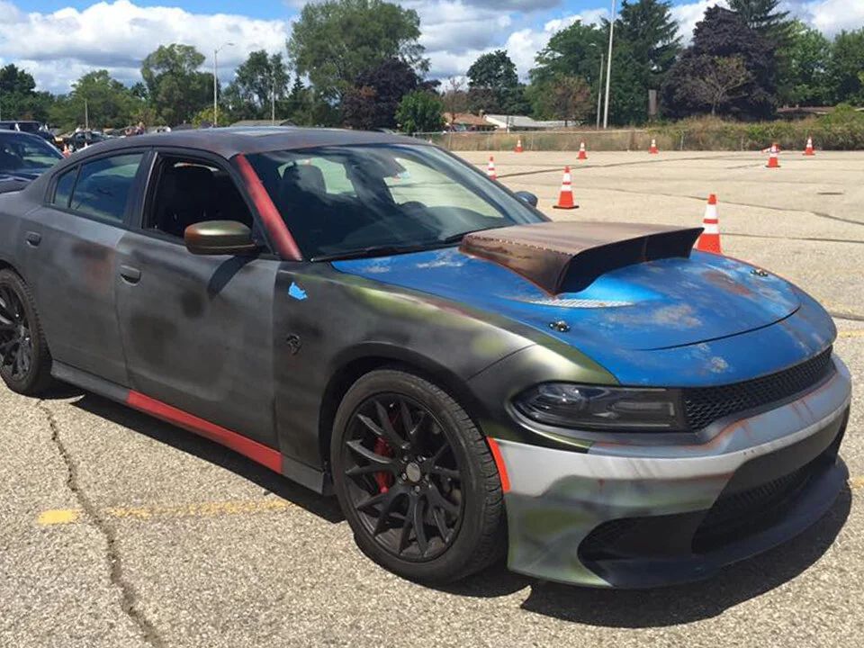 Matte black and blue Dodge Charger on a track with orange cones and a hood scoop