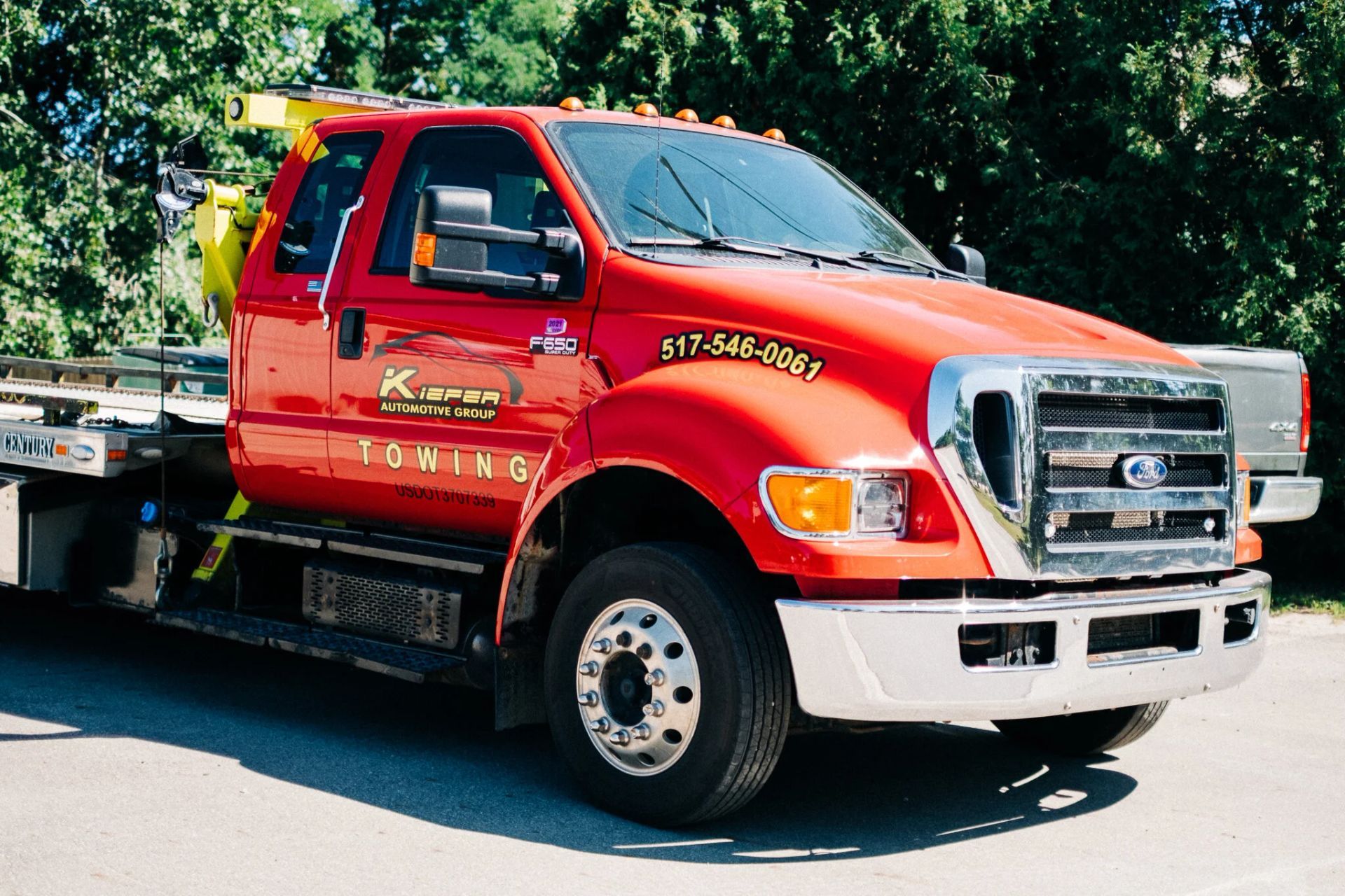 Red flatbed tow truck parked on a sunny street with trees in the background