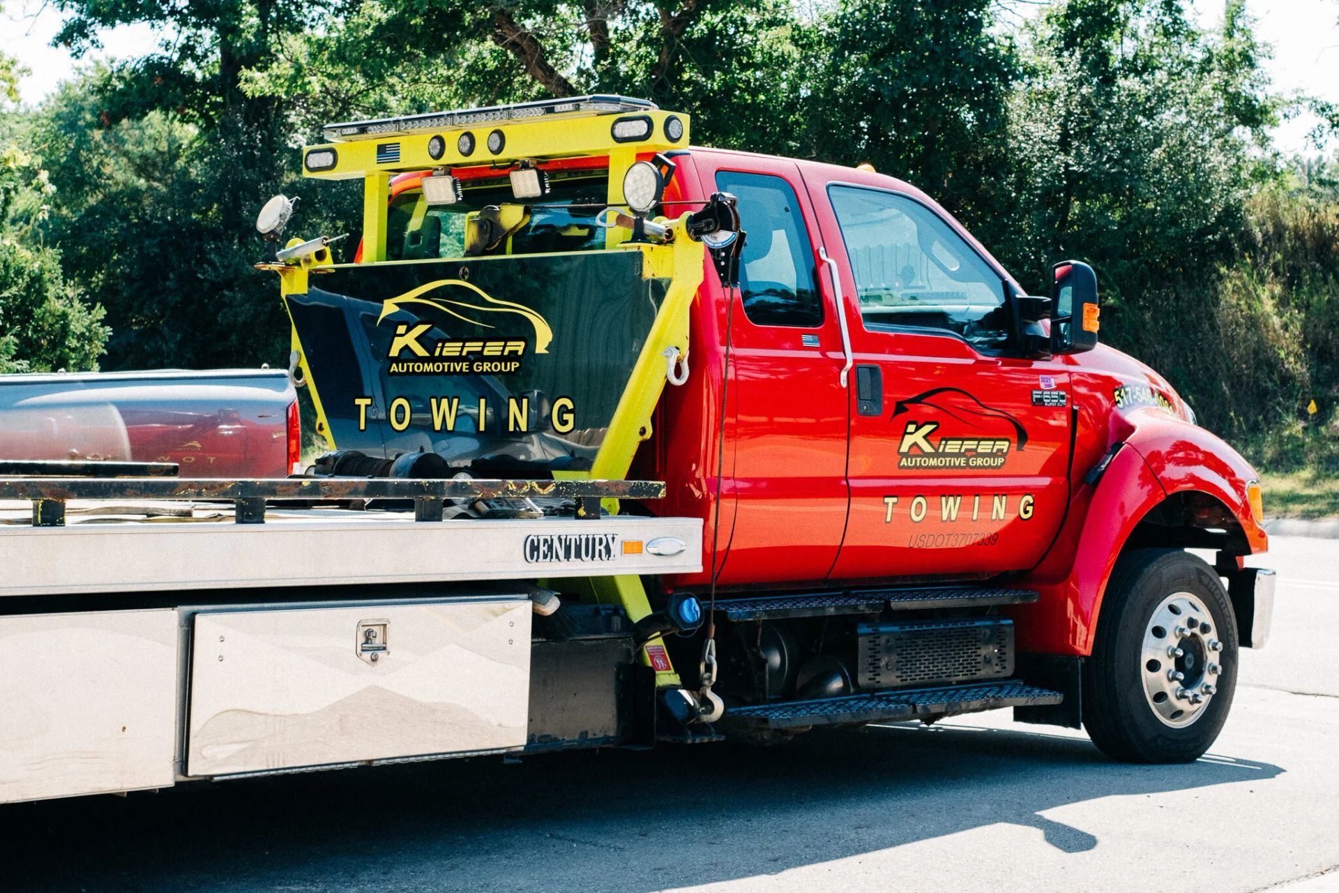 Red tow truck hauling a silver car on a flatbed trailer by the roadside.