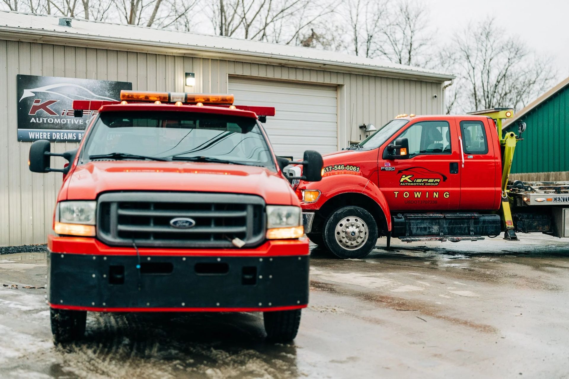 Two red emergency trucks parked outside a garage on a wet day