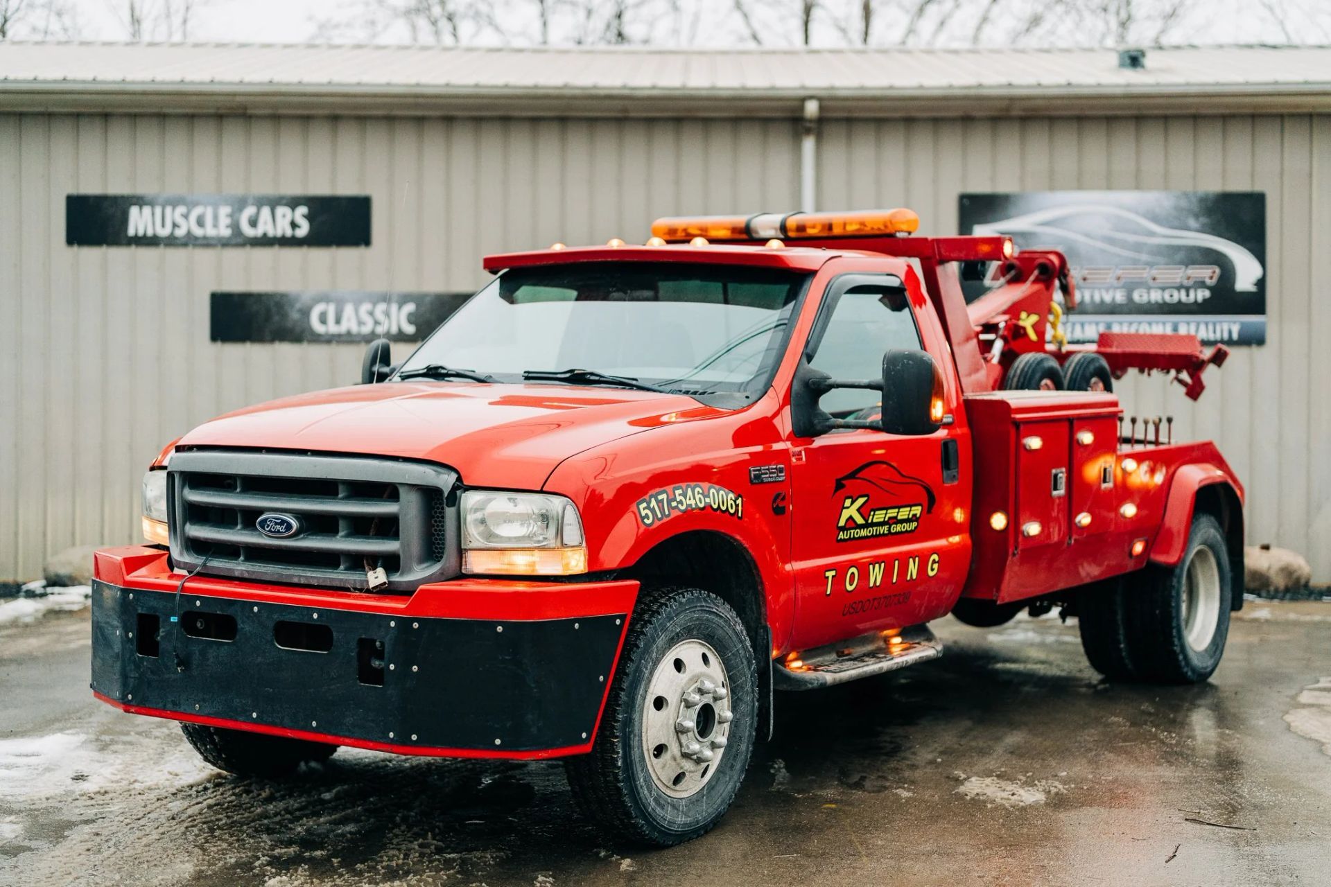 Red tow truck parked outside a classic car shop on a wet street