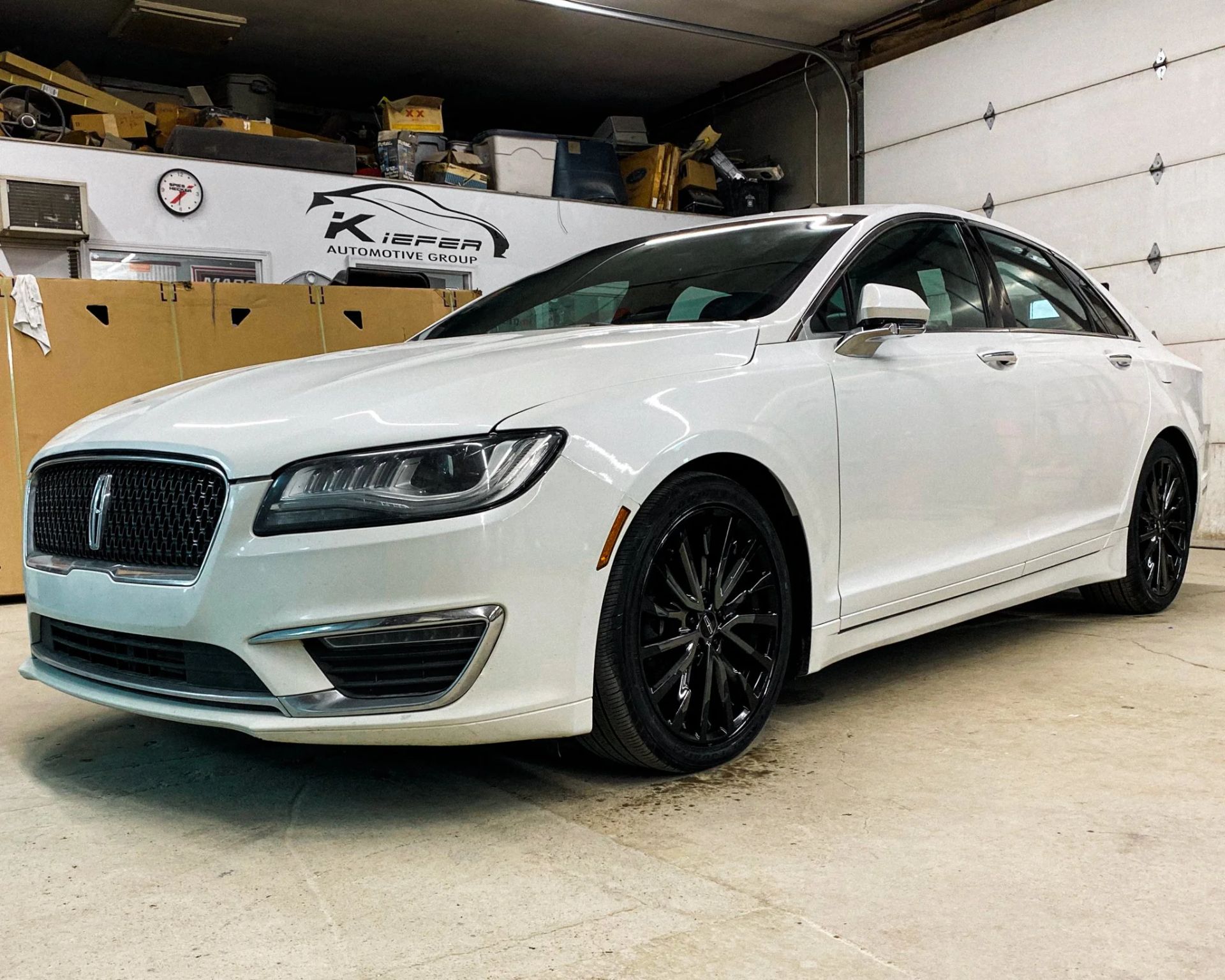 White luxury sedan parked in a garage, front three-quarter view, with black wheels.