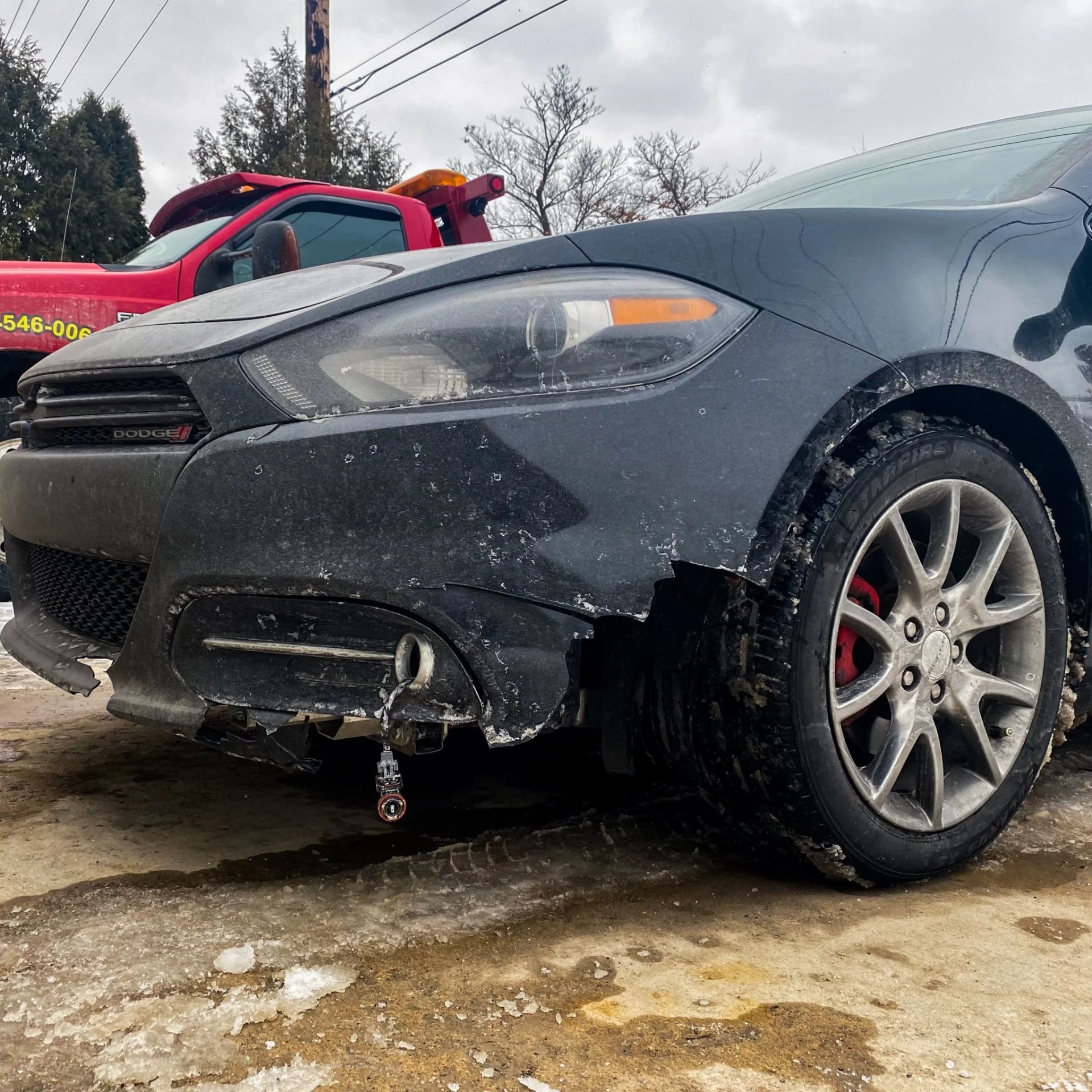 Damaged black sedan with front-end damage and flat tire on a slushy roadside