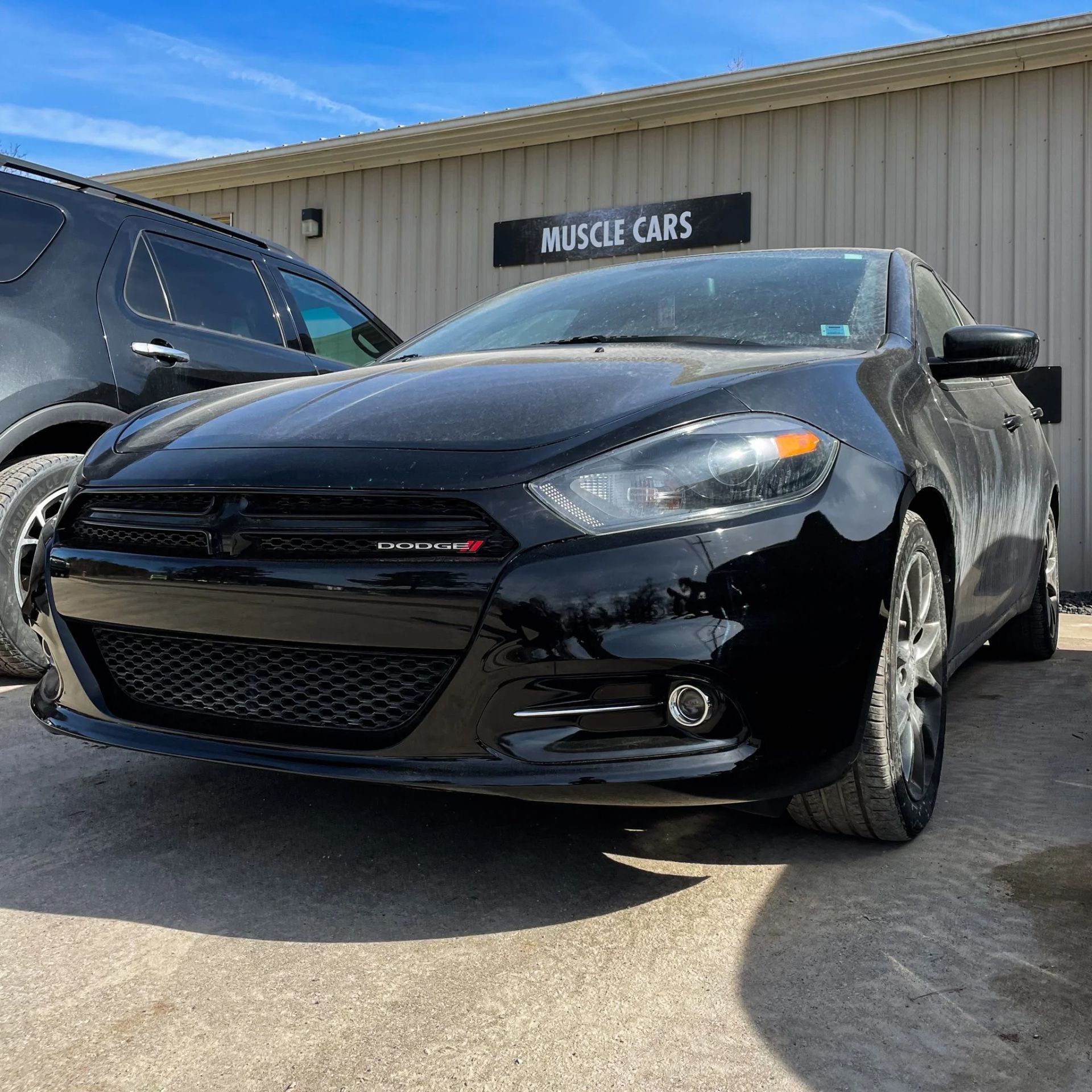 Black Dodge Charger parked outside a Muscle Cars dealership on a sunny day