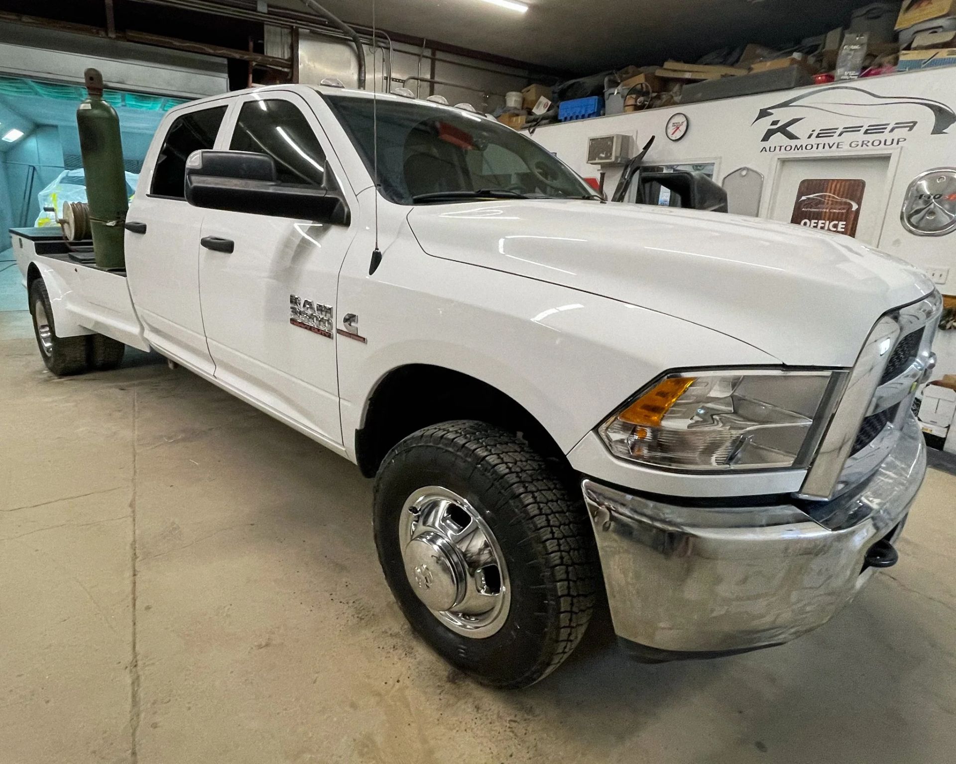 White heavy-duty pickup truck in an auto shop garage, angled front view, with chrome bumper and utility bed.