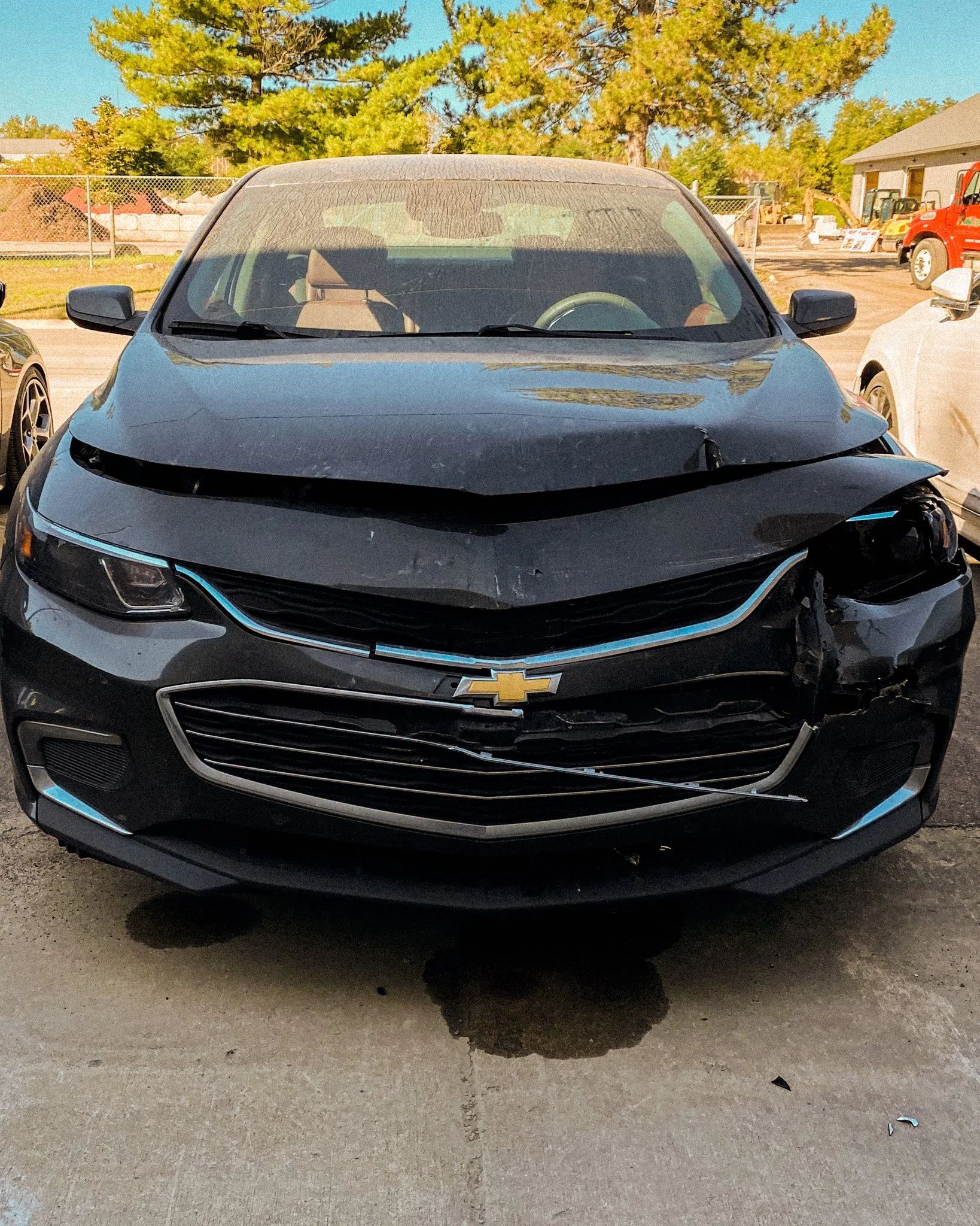 Front view of a black Chevrolet sedan with a crushed hood parked on a street.