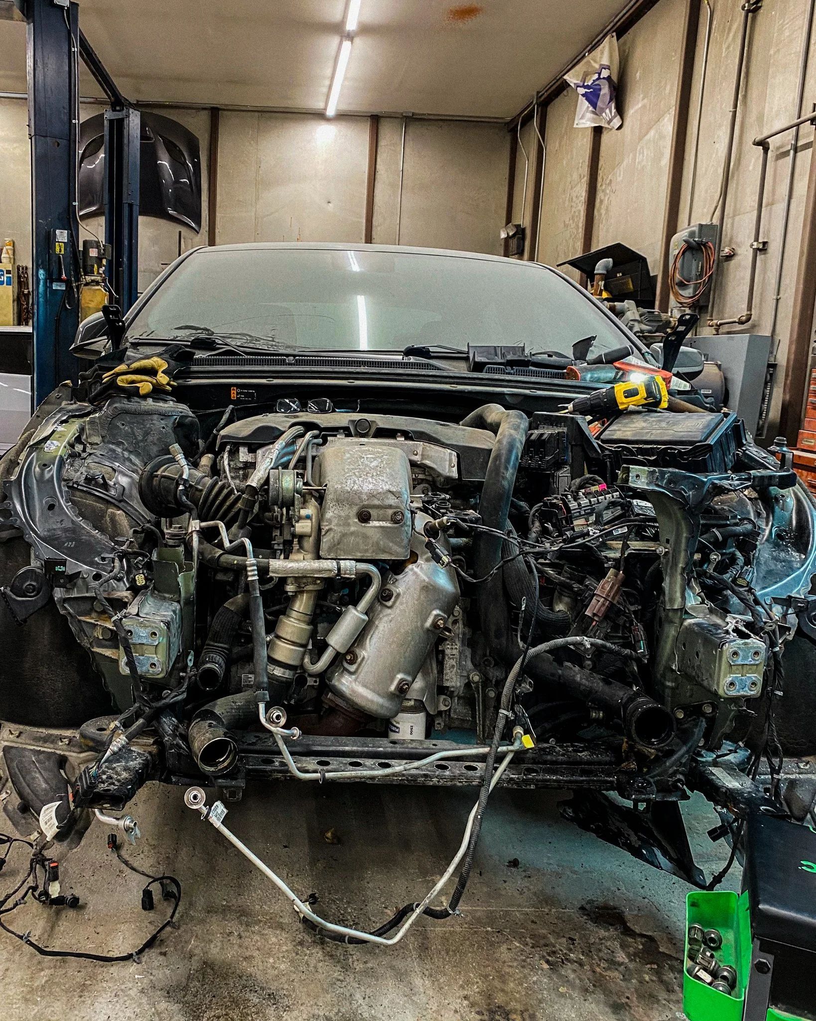 Severely damaged car front in a workshop, exposed engine and body panels removed.