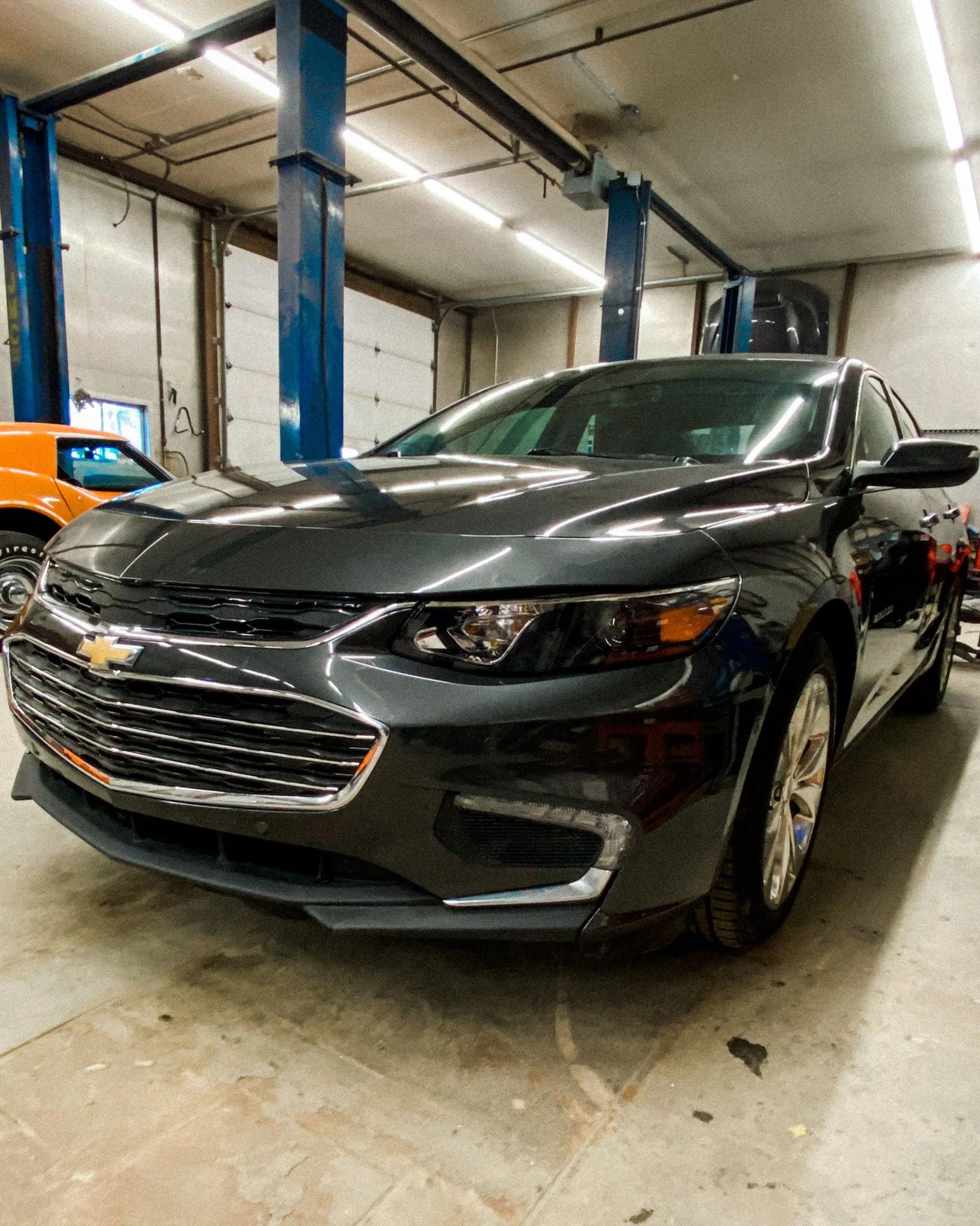 Dark gray sedan parked indoors in a garage with blue support columns