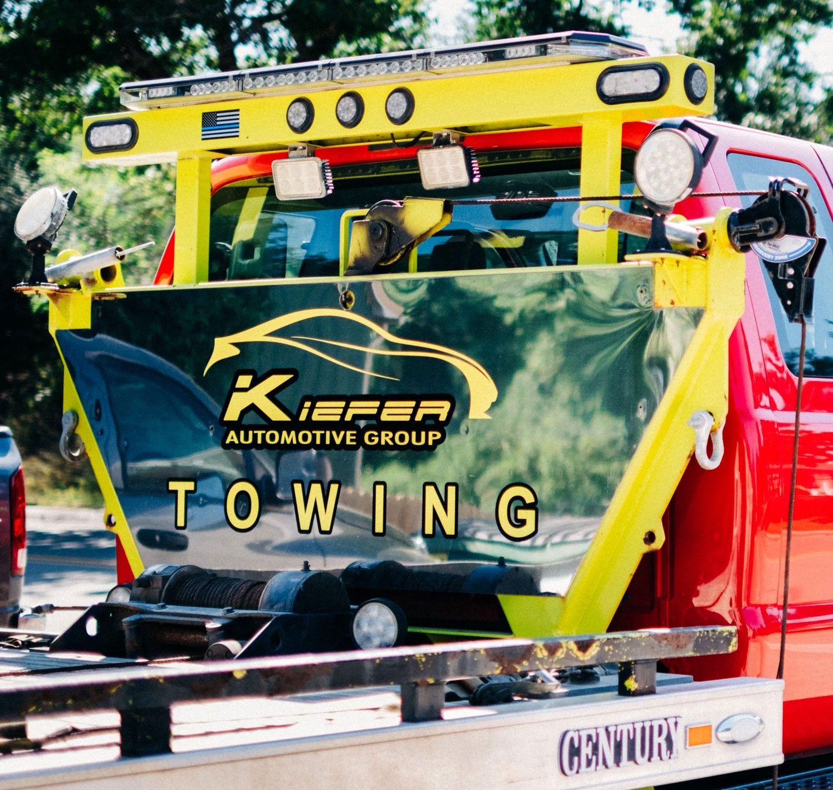 Tow truck with yellow lift carrying a green “K Automotive Group Towing” banner and car on the road