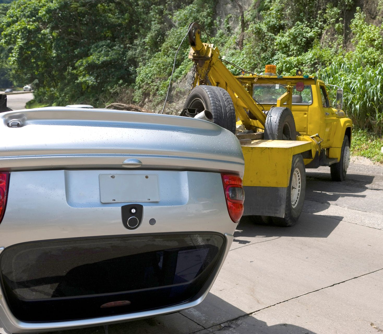 Silver car being towed by yellow tow truck on a road.