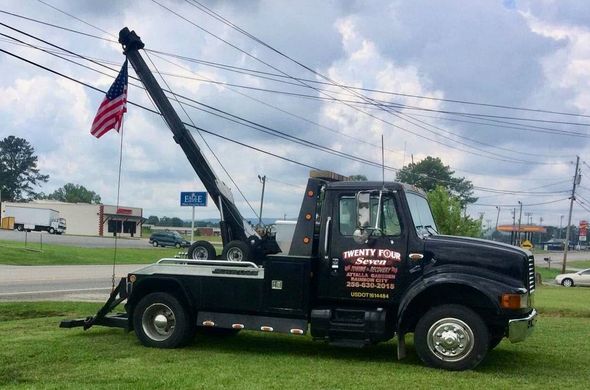 Black tow truck on grass with American flag; roadside setting.