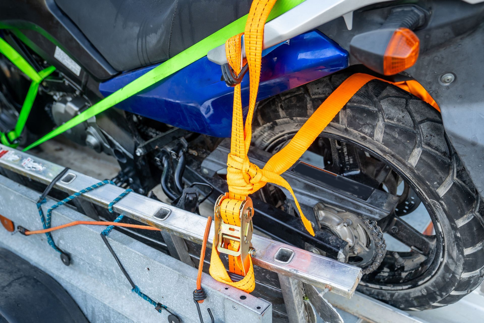 Motorcycle secured to a trailer with orange and green straps.
