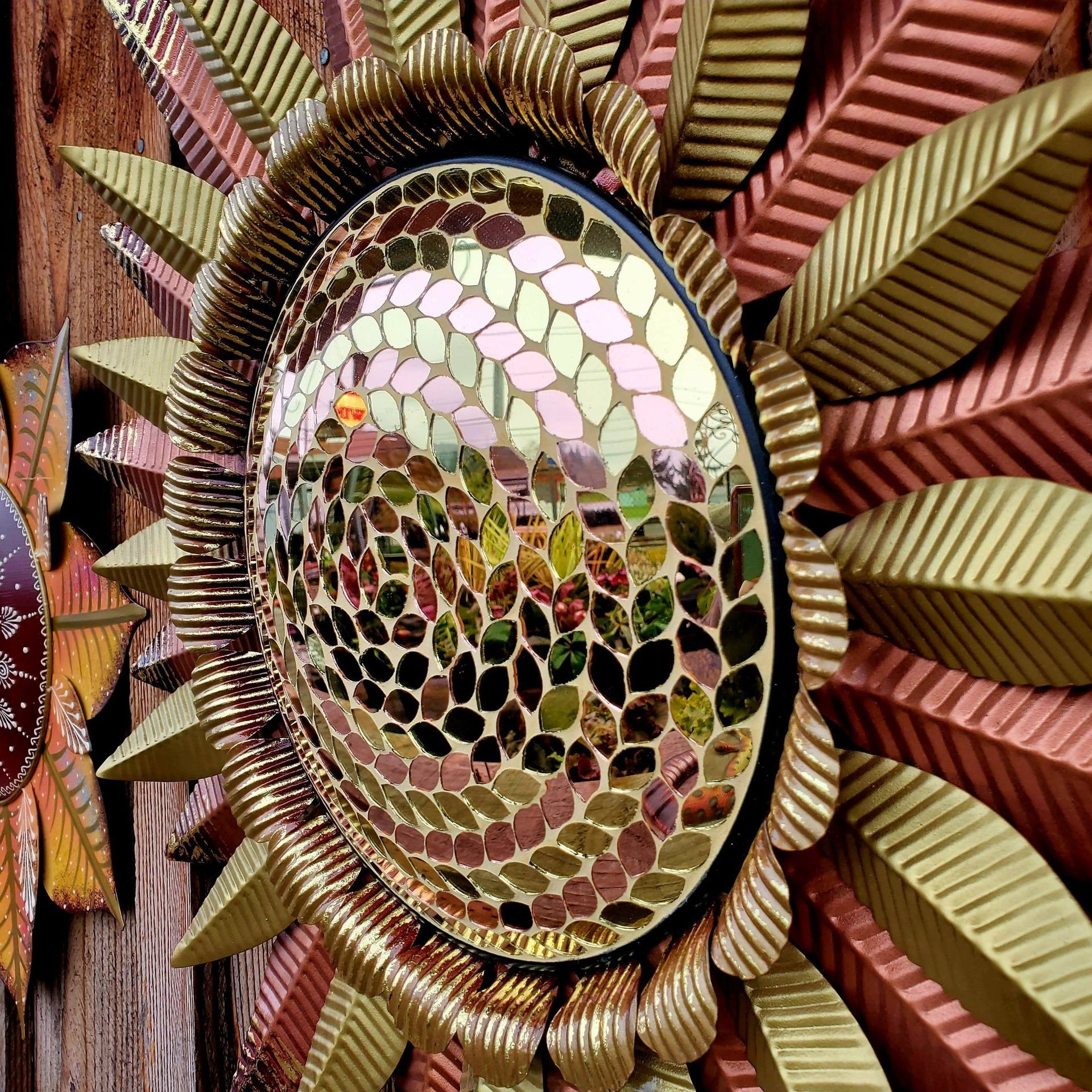 A decorative sun-shaped wall art piece with a mosaic mirror center surrounded by metallic gold and copper leaves.