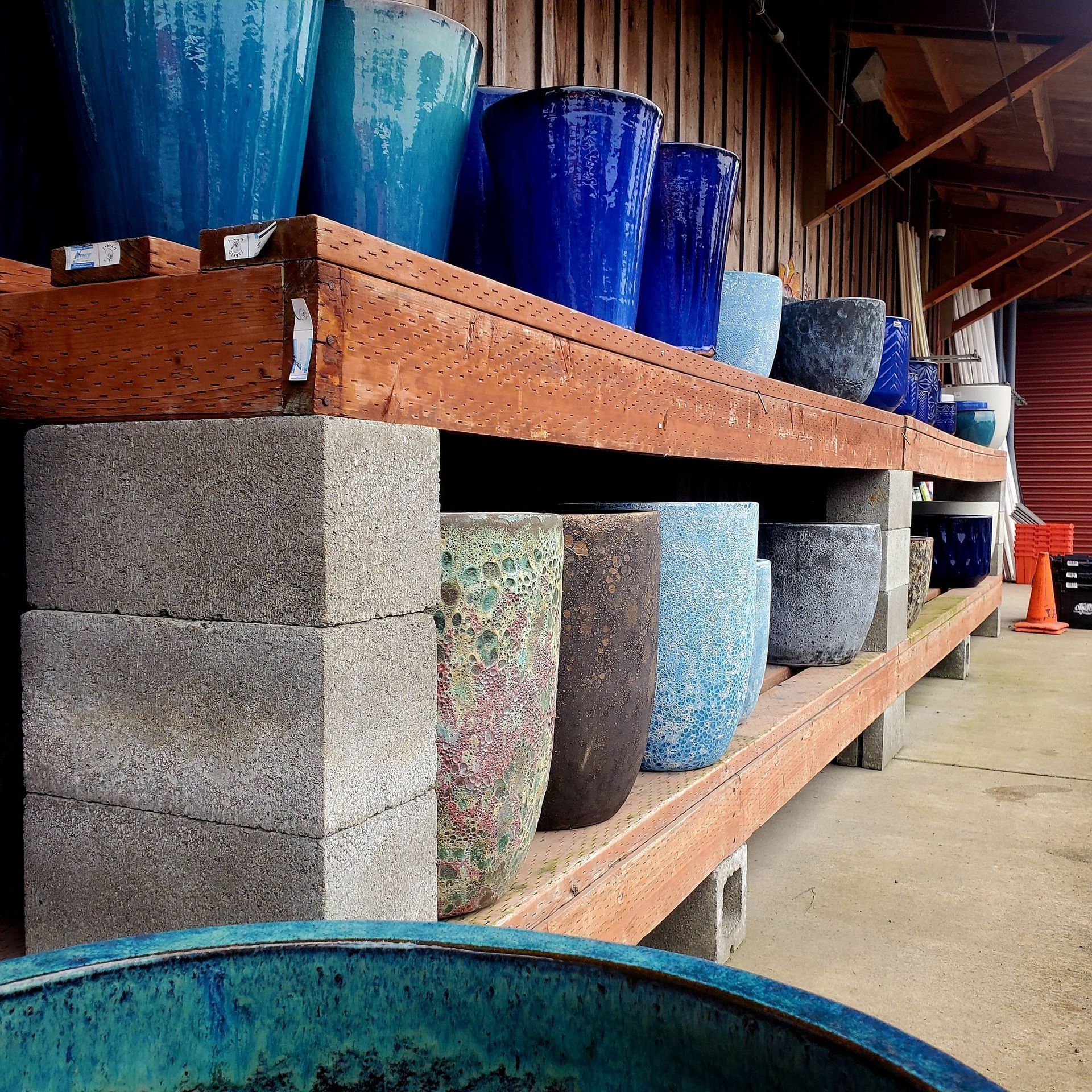 Ceramic garden pots in various colors and textures displayed on wooden shelves supported by concrete blocks.