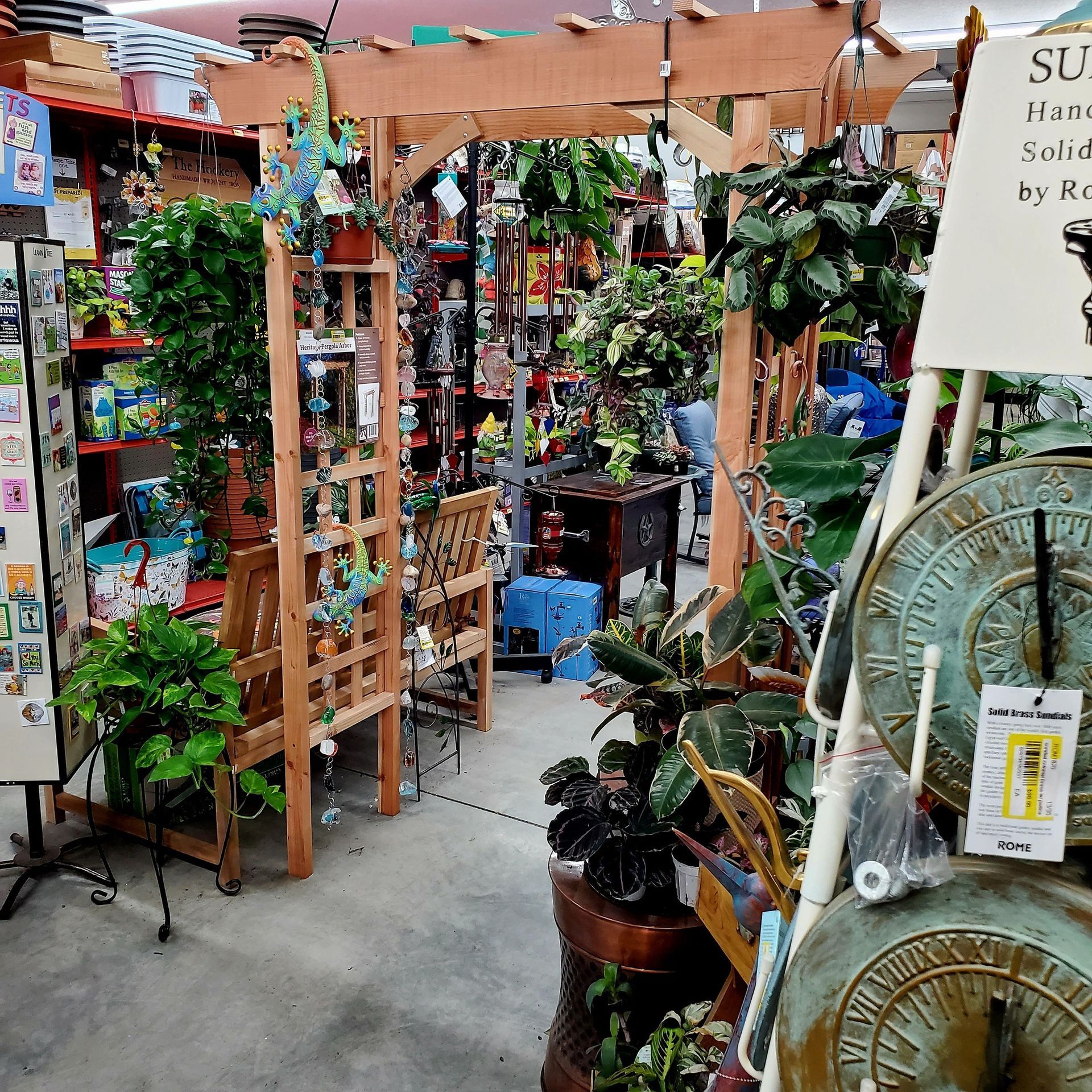 A garden shop display featuring wooden trellis arches, hanging plants, and metal sundials for sale.