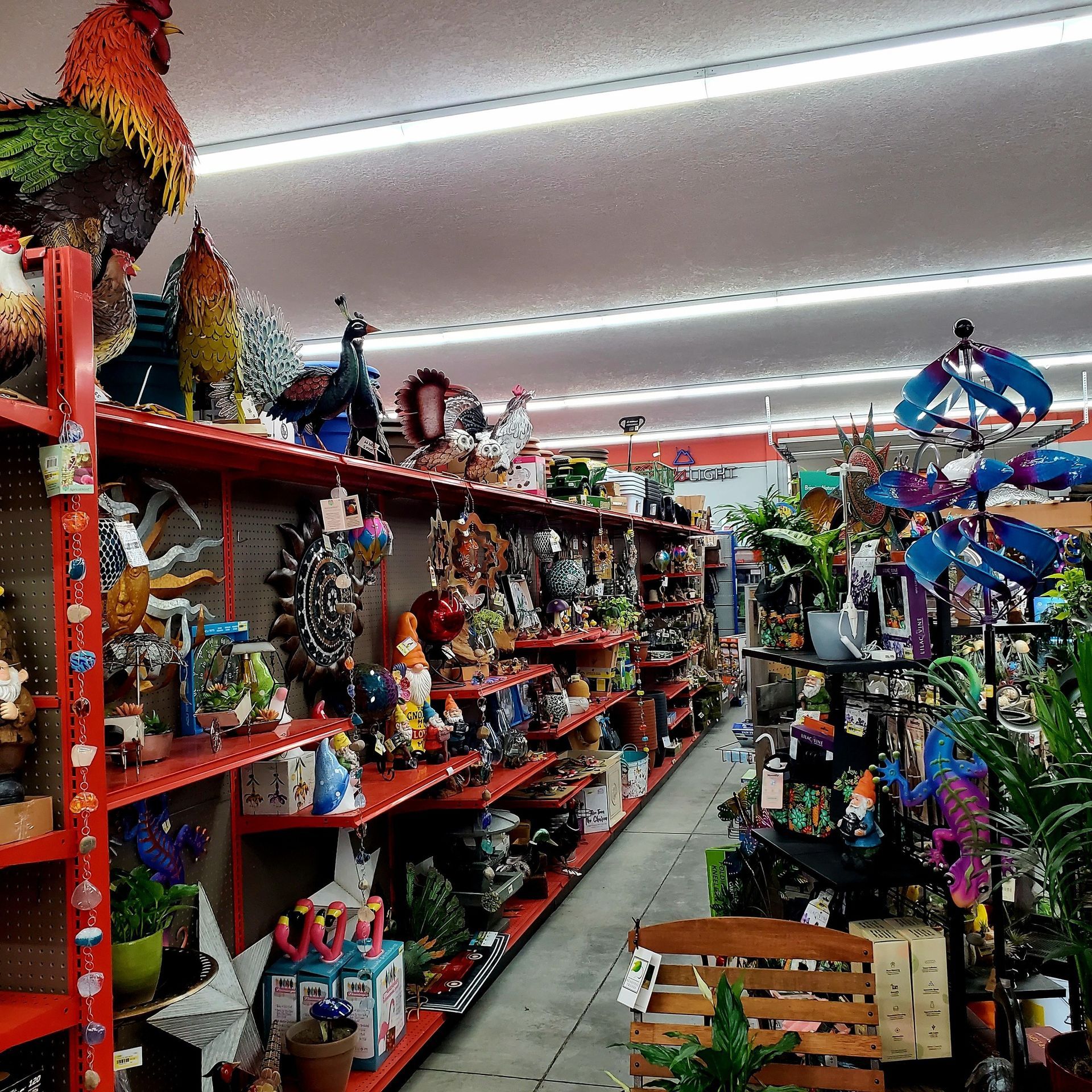 Shelves inside a store are filled with colorful garden decor, including metal roosters, ornaments, and wind spinners.