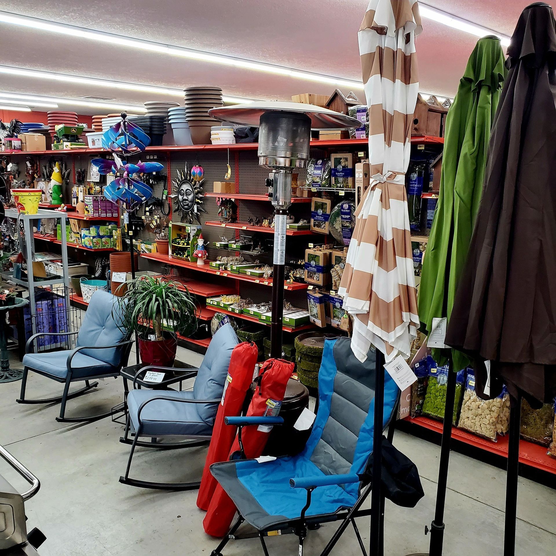 A retail store aisle filled with outdoor living items, including rocking chairs, folding chairs, and umbrellas.