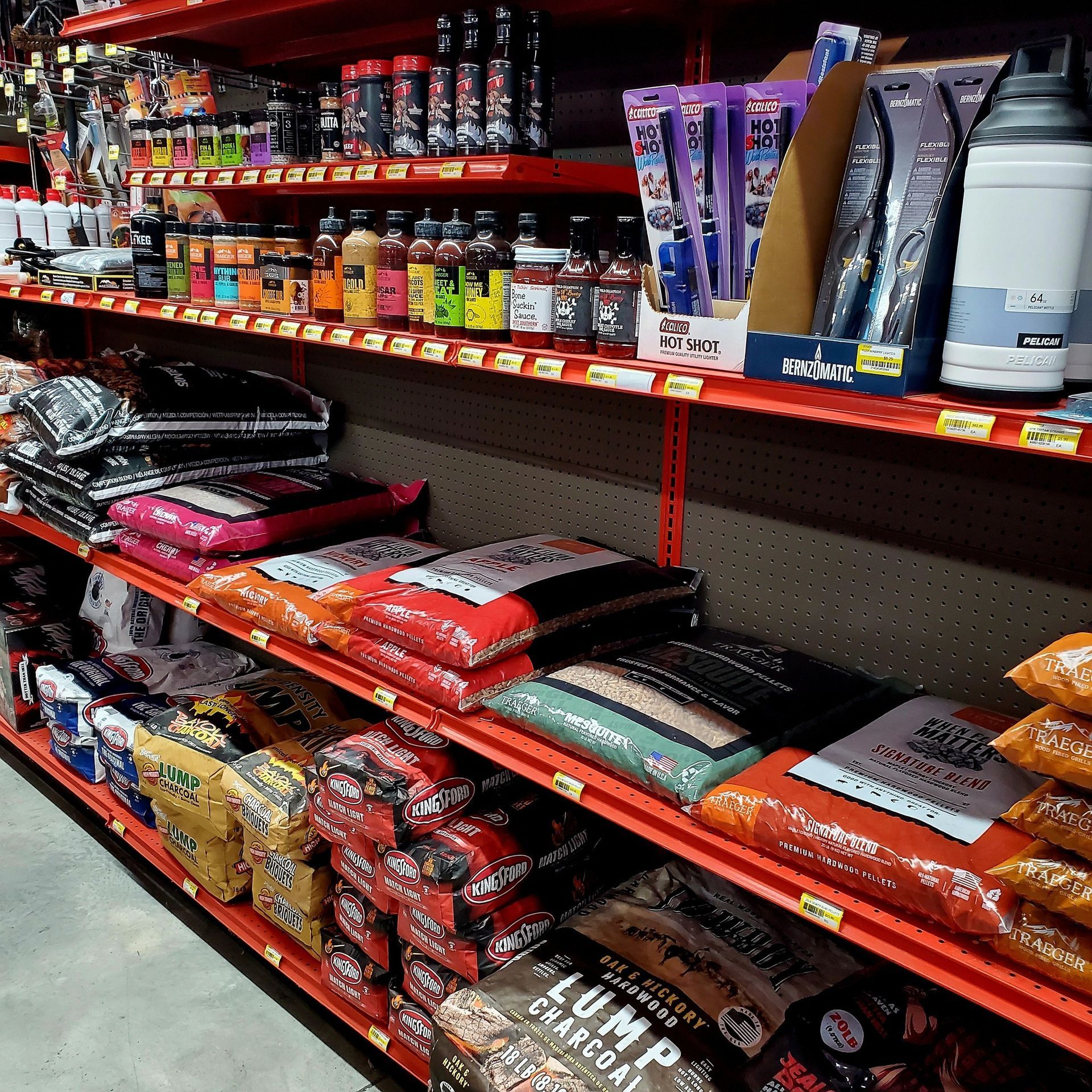 Shelves in a retail store stocked with various BBQ charcoal bags and grilling accessories.