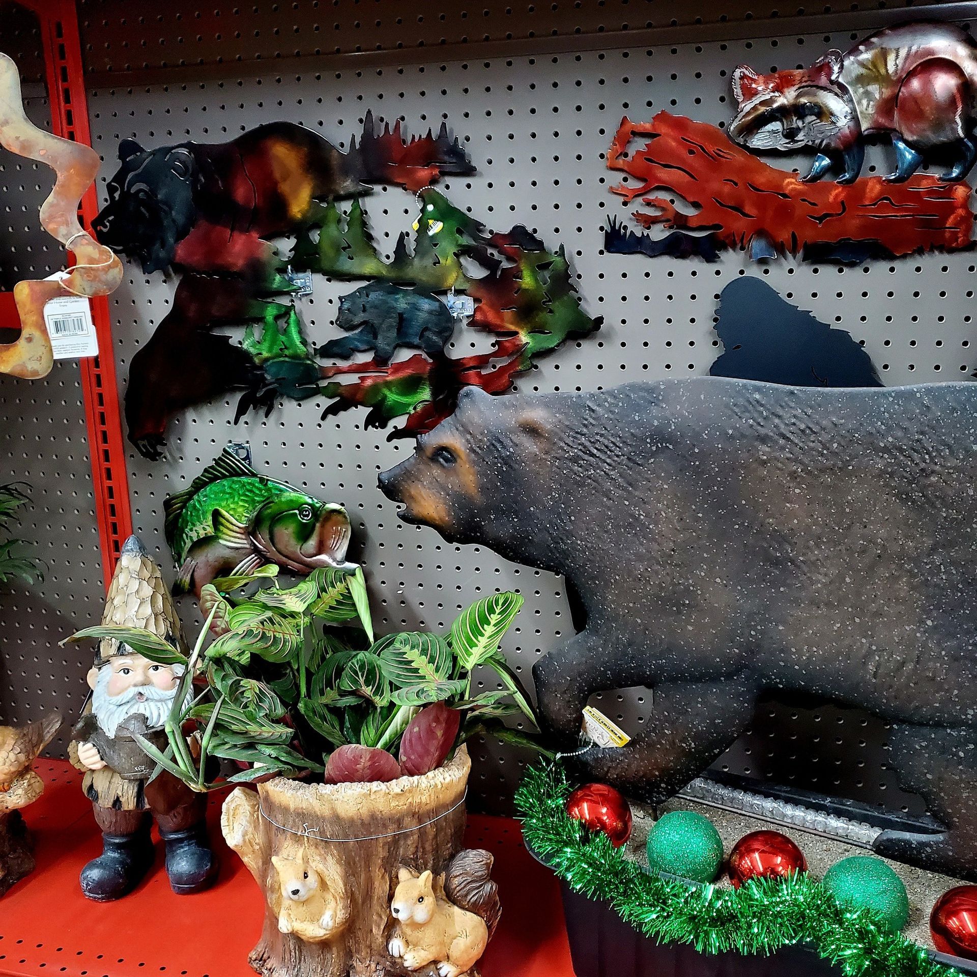 Rustic retail display featuring decorative metal wildlife wall art, a gnome figurine, squirrel planter, and a large bear.