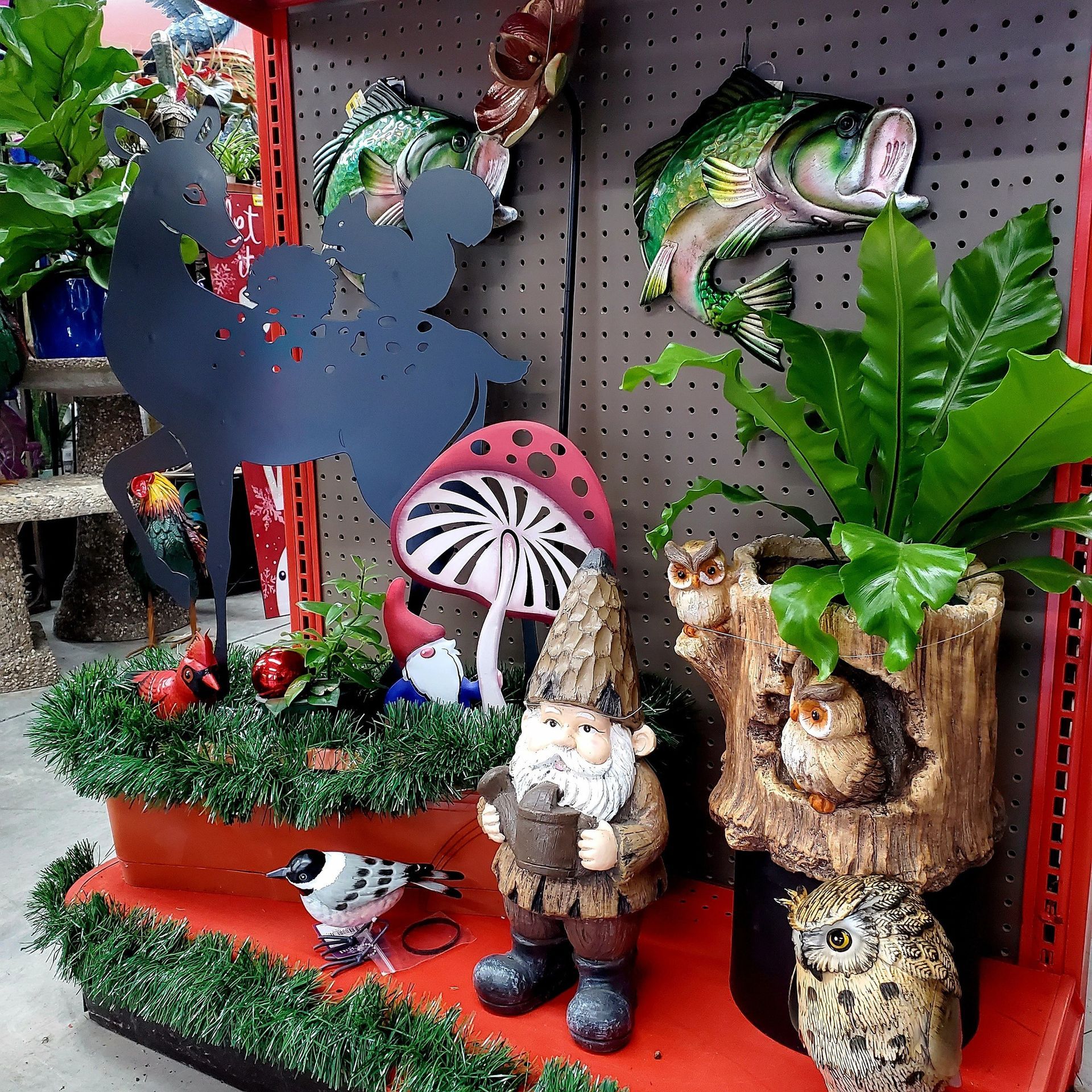 A retail shelf display features garden decor including a metal deer, a gnome, a mushroom, bird figurines, and an owl planter.