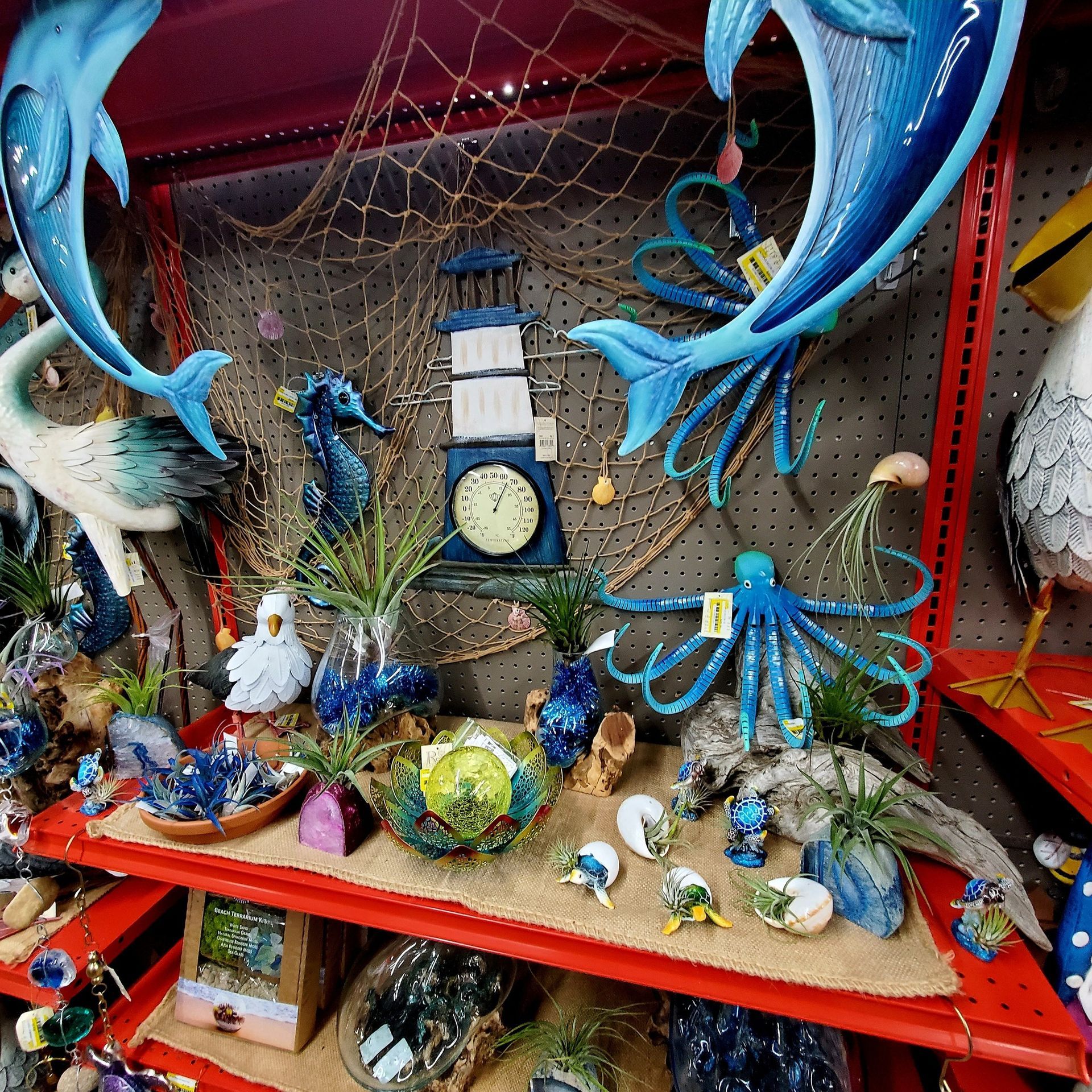 A store shelf displays nautical-themed metal decor, including dolphins, a lighthouse, a seahorse, and an octopus.