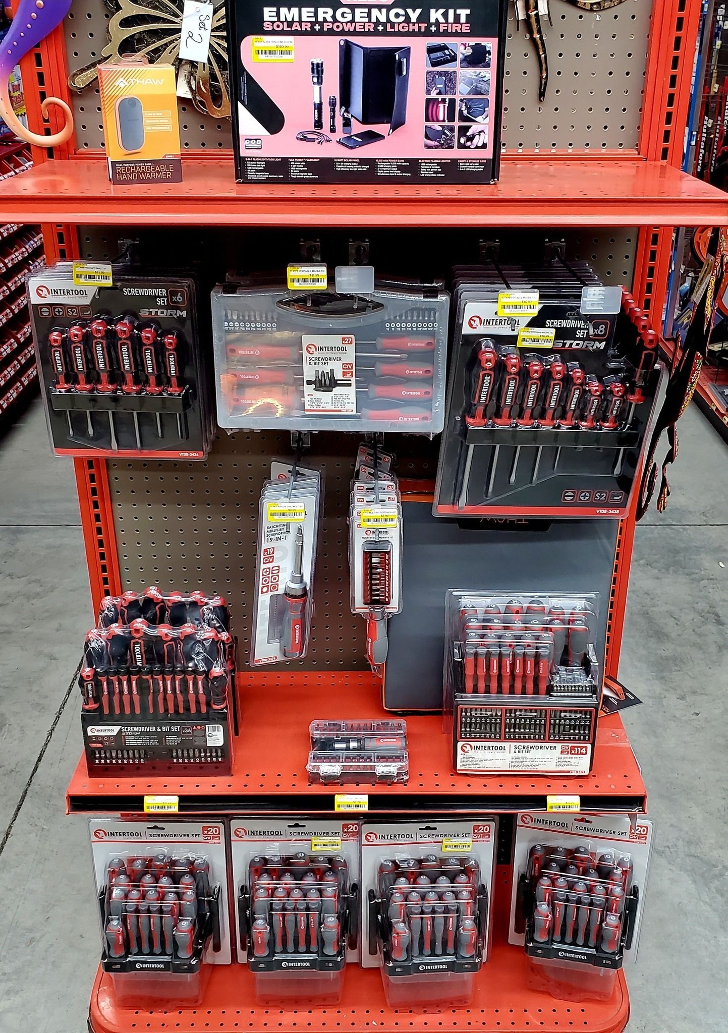 A store display of various red-handled hand tool sets and an emergency kit on orange metal shelving.