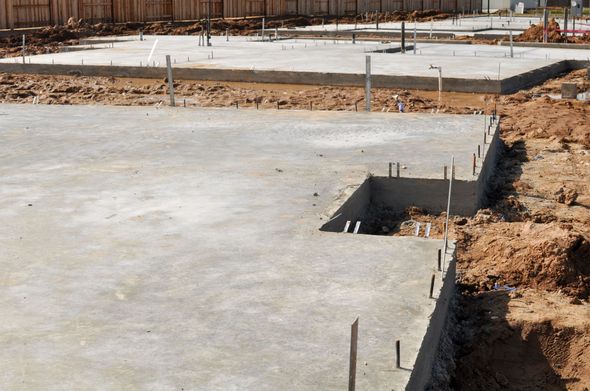Concrete foundations for multiple buildings under construction, with pipes and dirt visible.