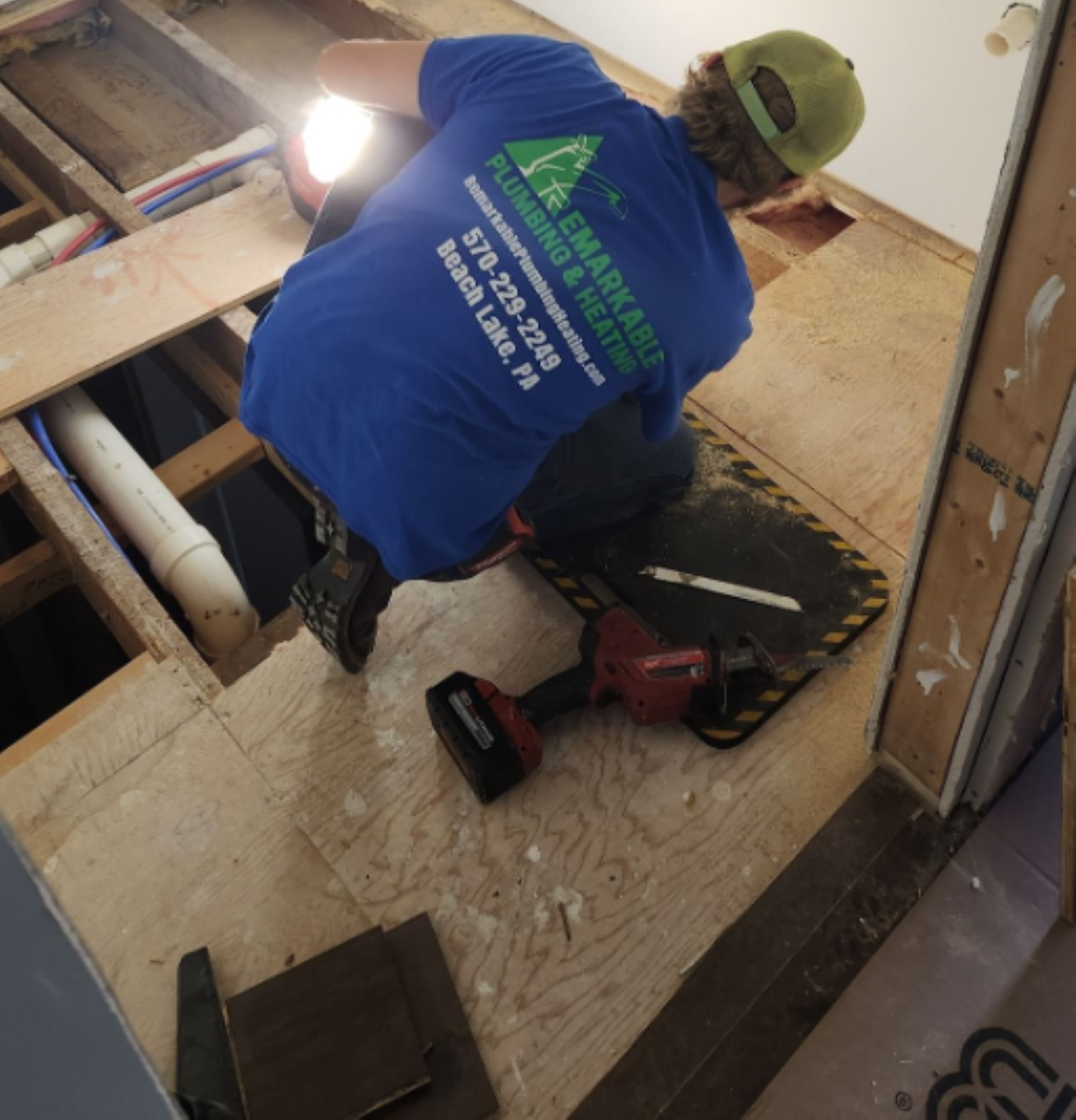 Person in blue shirt inspecting floor with flashlight. Interior view. Partially exposed floorboards.