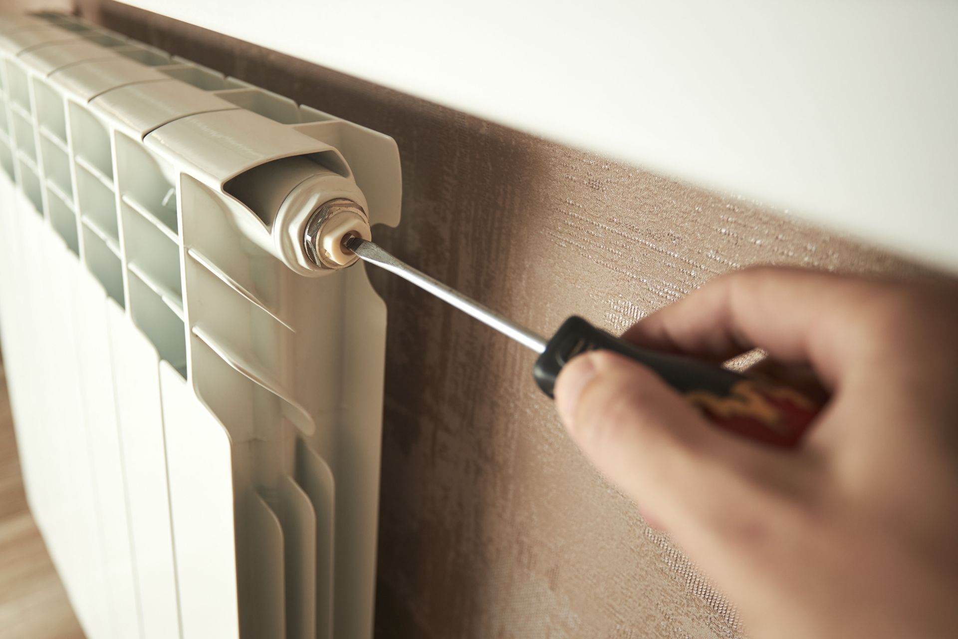 White radiator under a window in a room with dark wood floors and a light-colored wall.