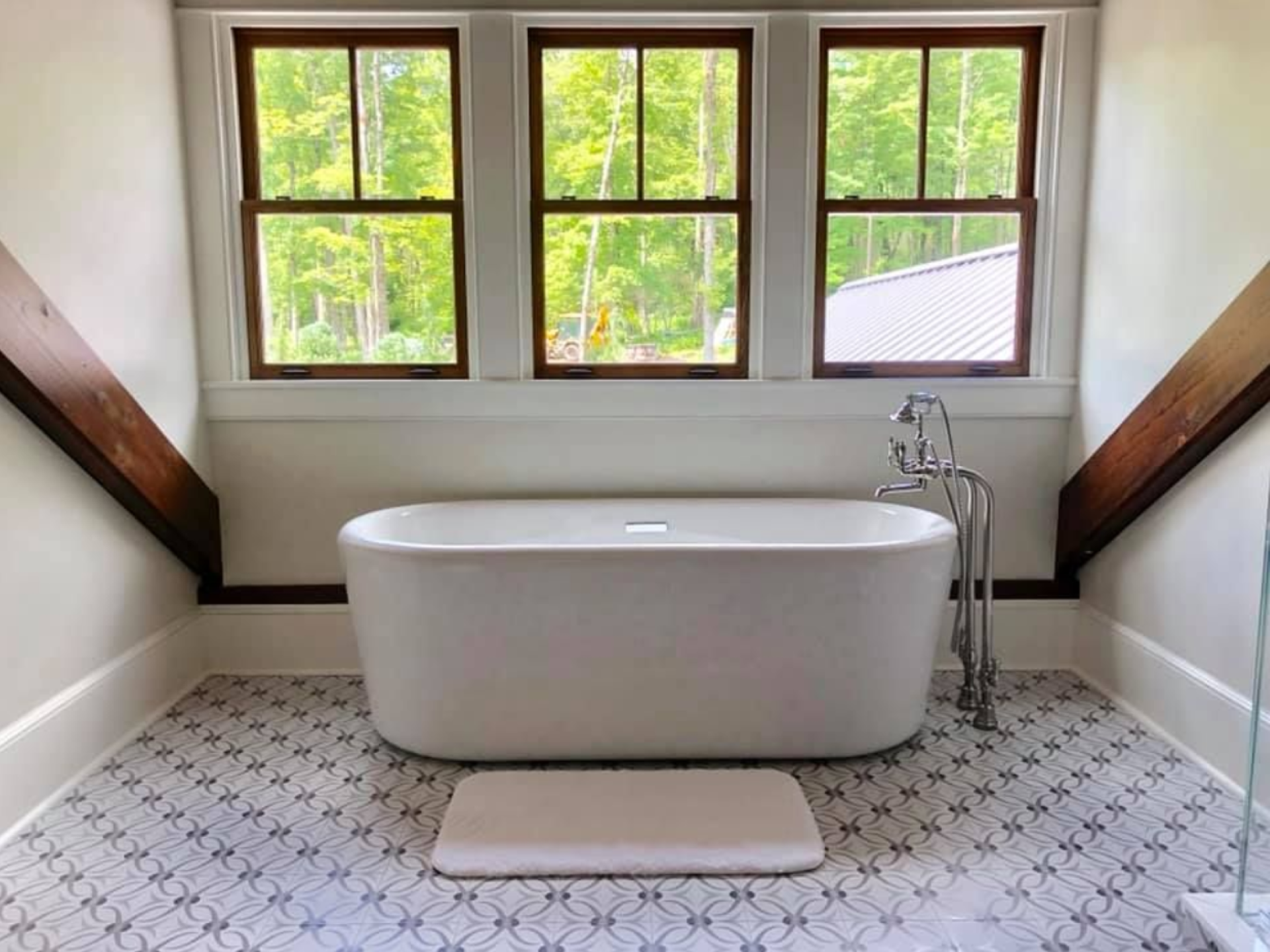Bathroom with white tub, three windows, patterned tile floor, and wooden beams.