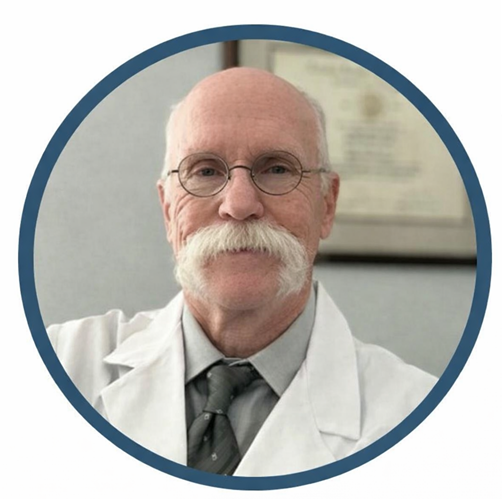 Older man in white lab coat, glasses, and large white mustache, likely a doctor.