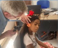 A person examining a child's ear with an otoscope. The child has long hair and a red bow.